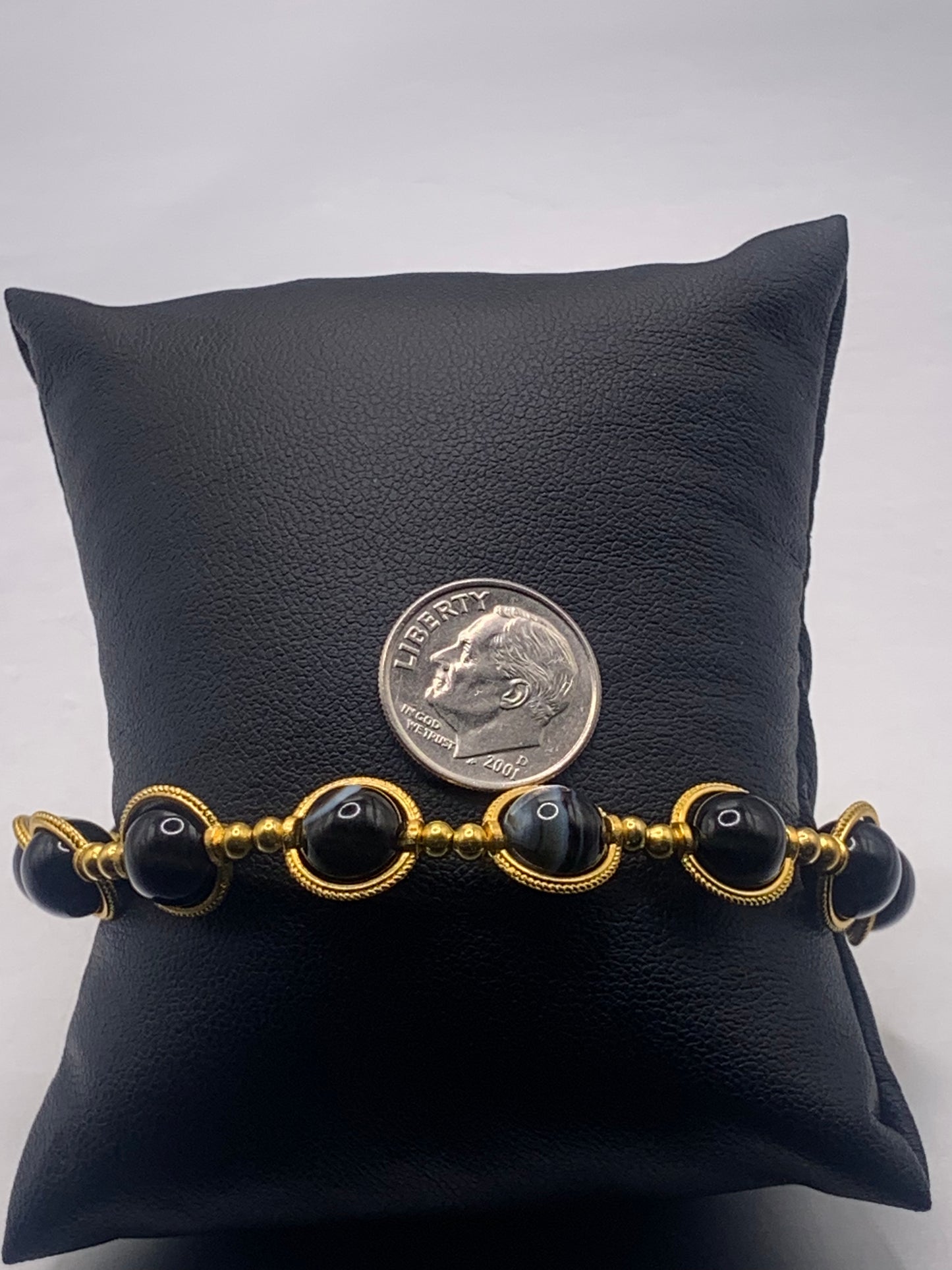 Bracelet with black lace agate beads and gold accents on a black cushion, with a dime for scale.
