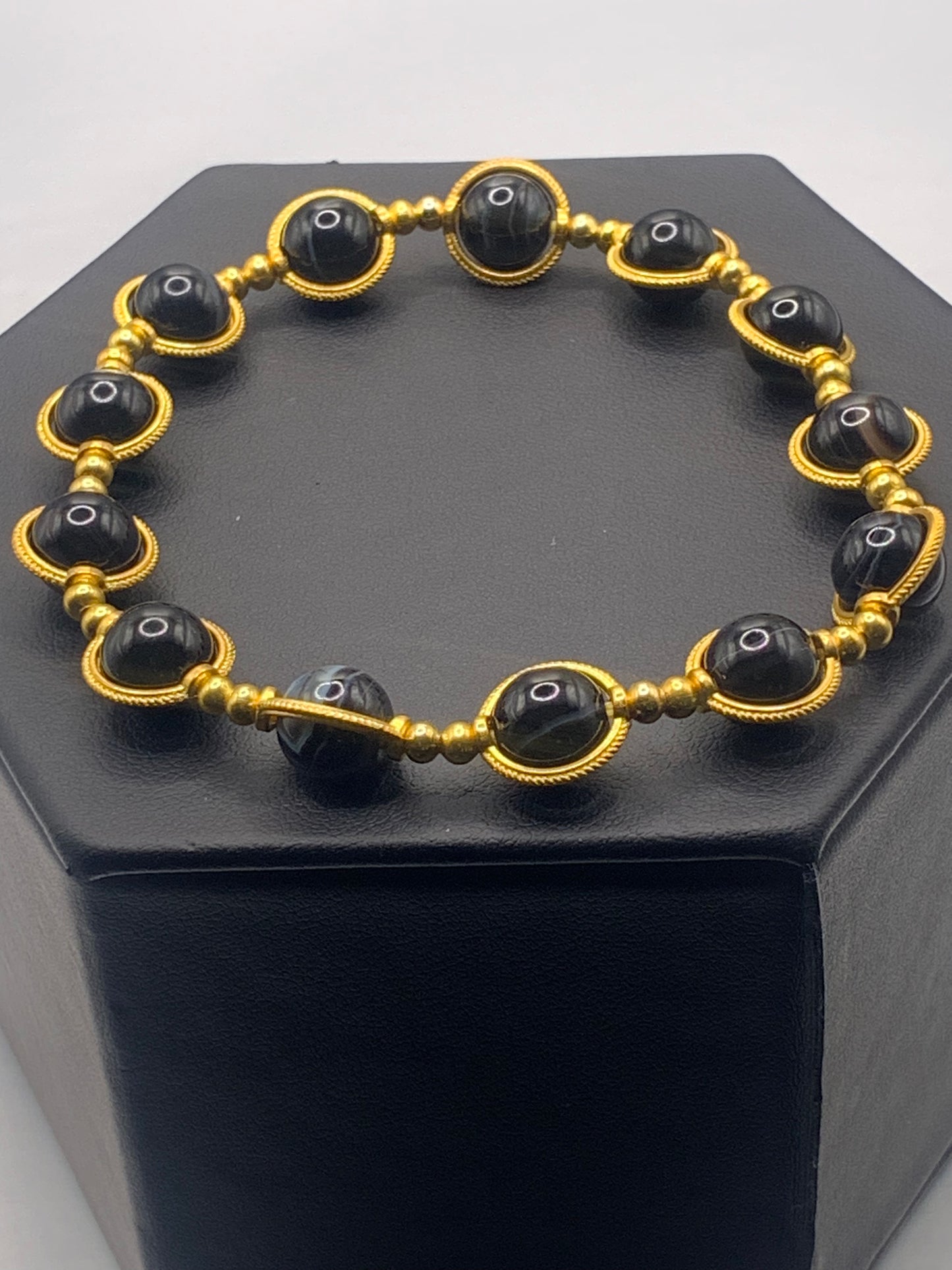 Black lace agate beaded bracelet with gold accents on a black hexagonal stand