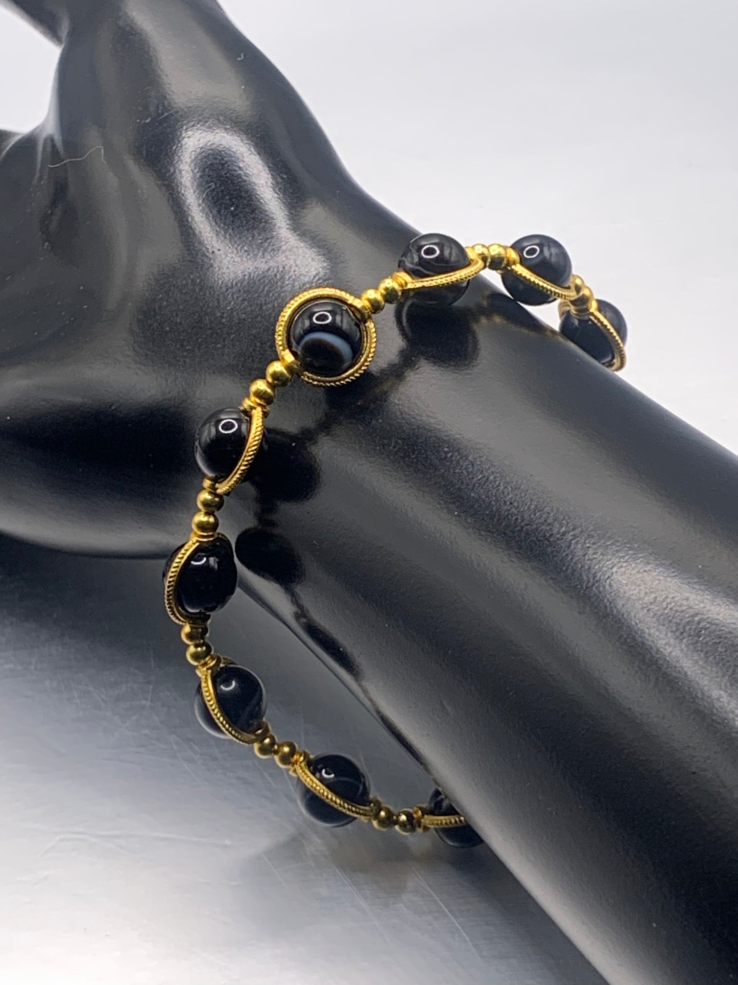 Black lace agate beaded bracelet with gold accents on a black mannequin hand against a white background
