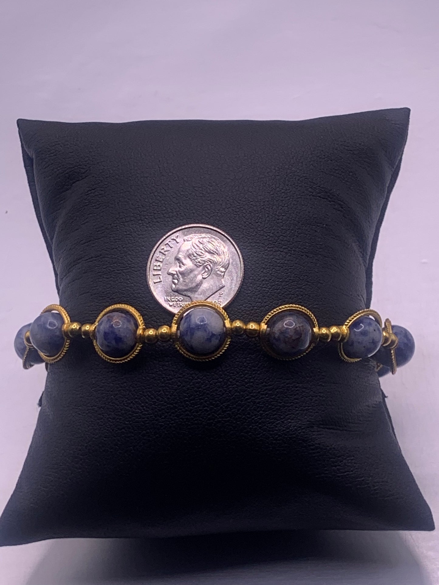 Bracelet with blue dot jasper stones and gold accents on a black pillow, dime for scale.