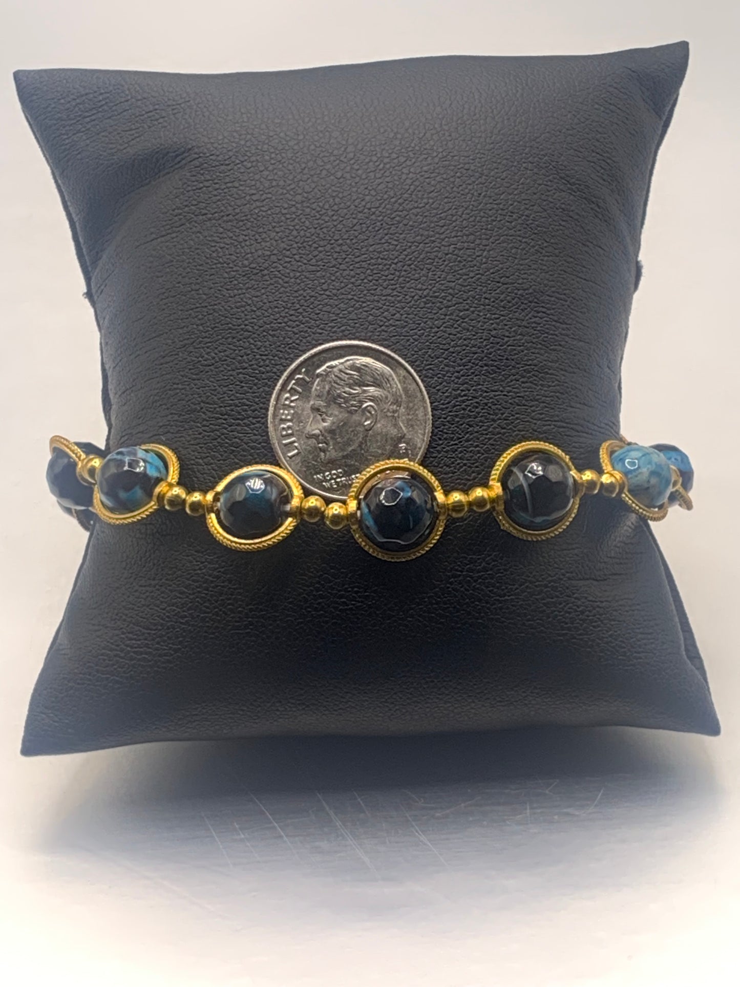 Bracelet with blue orca agate beads and gold accents on a gray pillow, with a coin for scale.