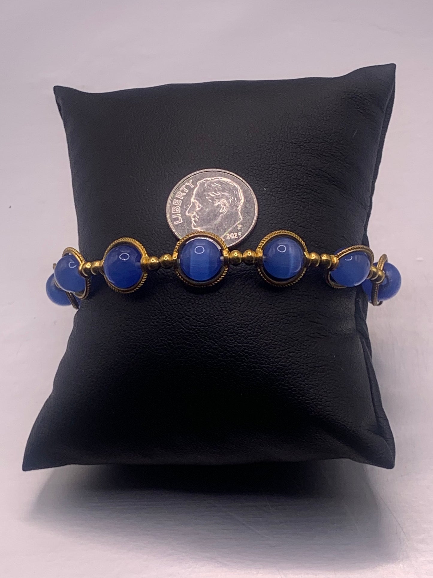 Bracelet with blue cats eye beads and gold accents on a black cushion, with a coin for scale.