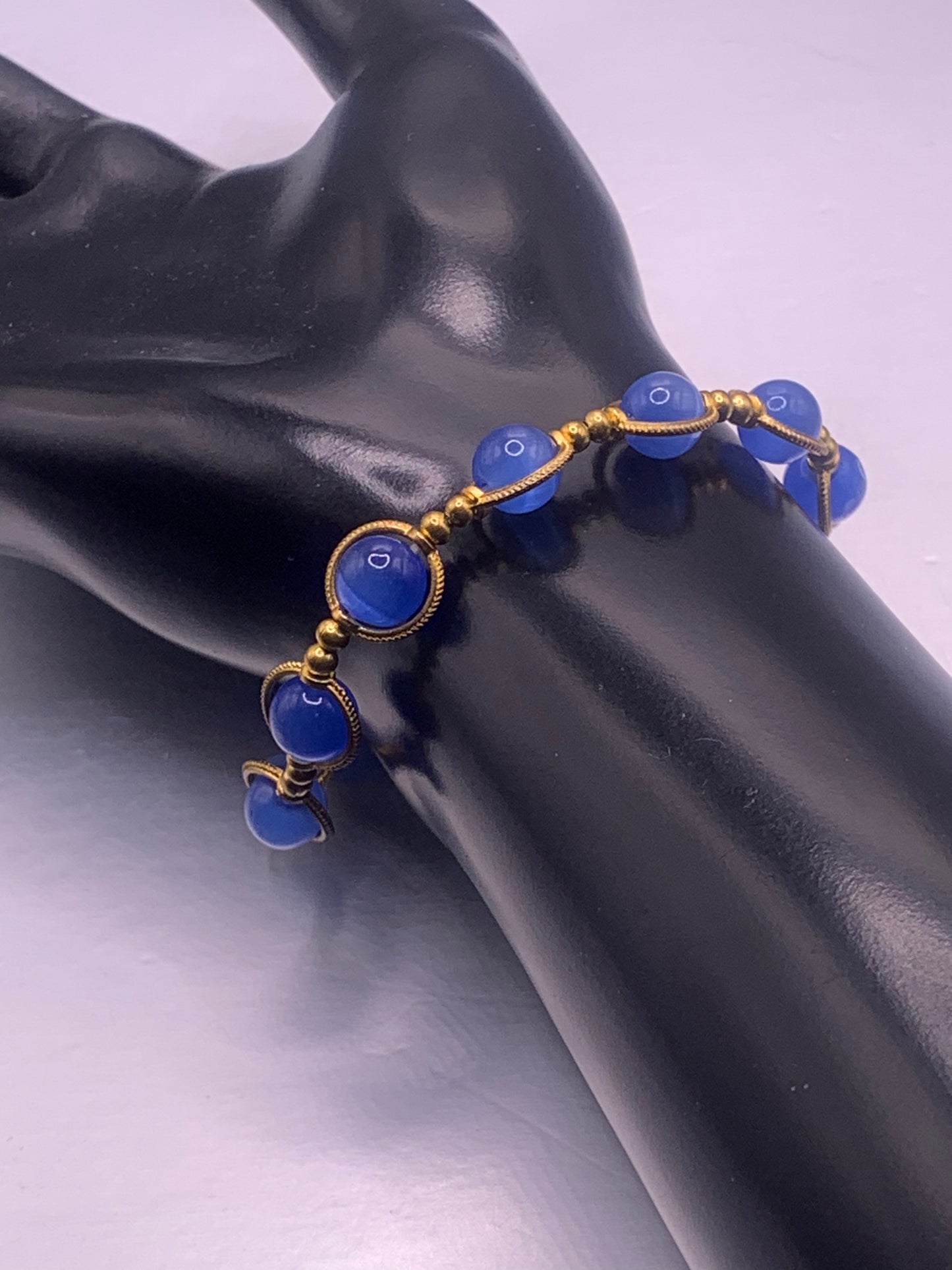 Blue cats eye beaded bracelet with gold accents on a black mannequin hand against a gray background