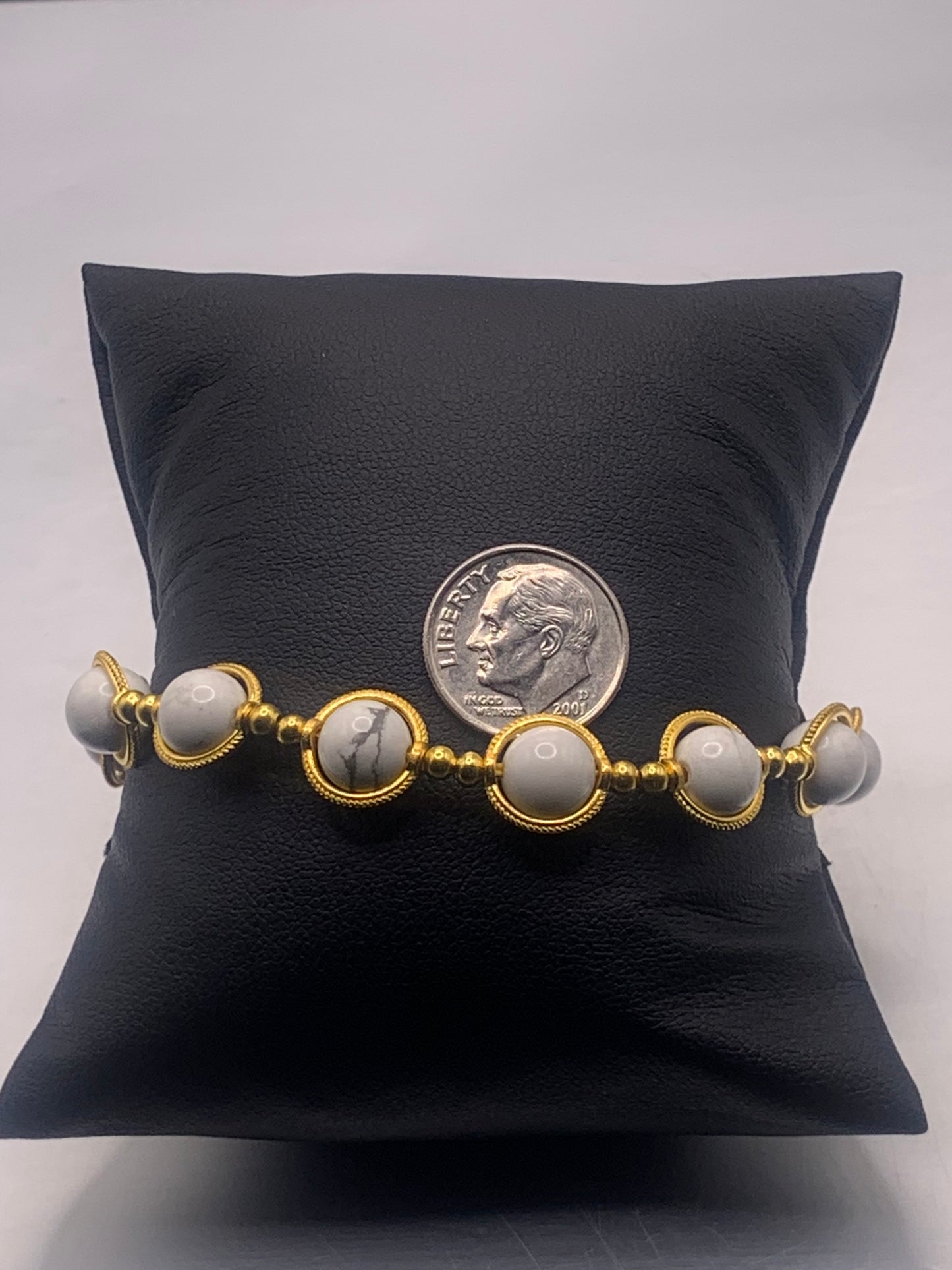 Bracelet with howlite beads and gold accents on a black pillow with a dime for scale