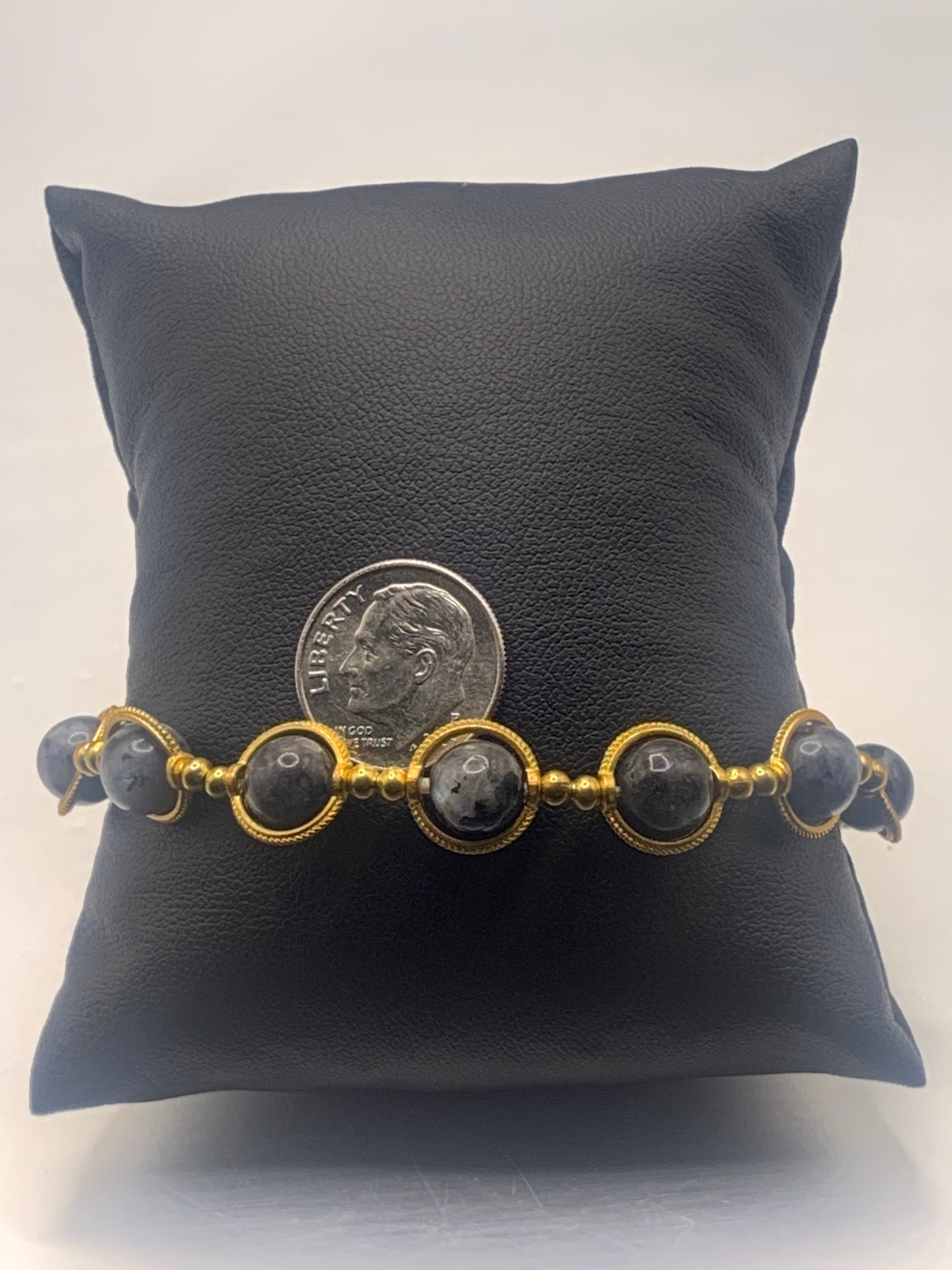 Bracelet with gold accents and larvikite beads on a black pillow, with a dime for scale.