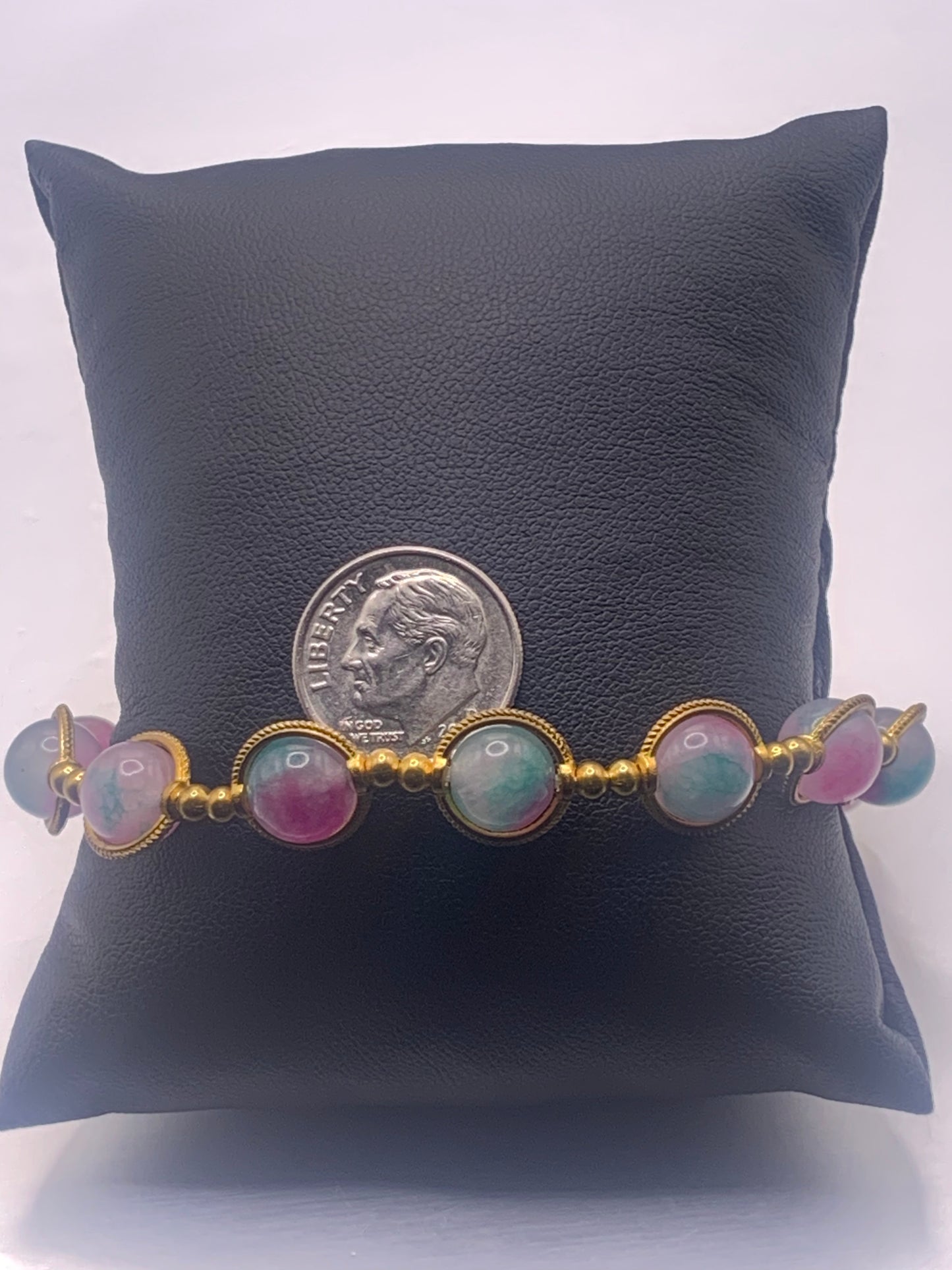 Bracelet with colorful teal and pink chalcedony beads and gold accents on a black pillow with a dime for scale.