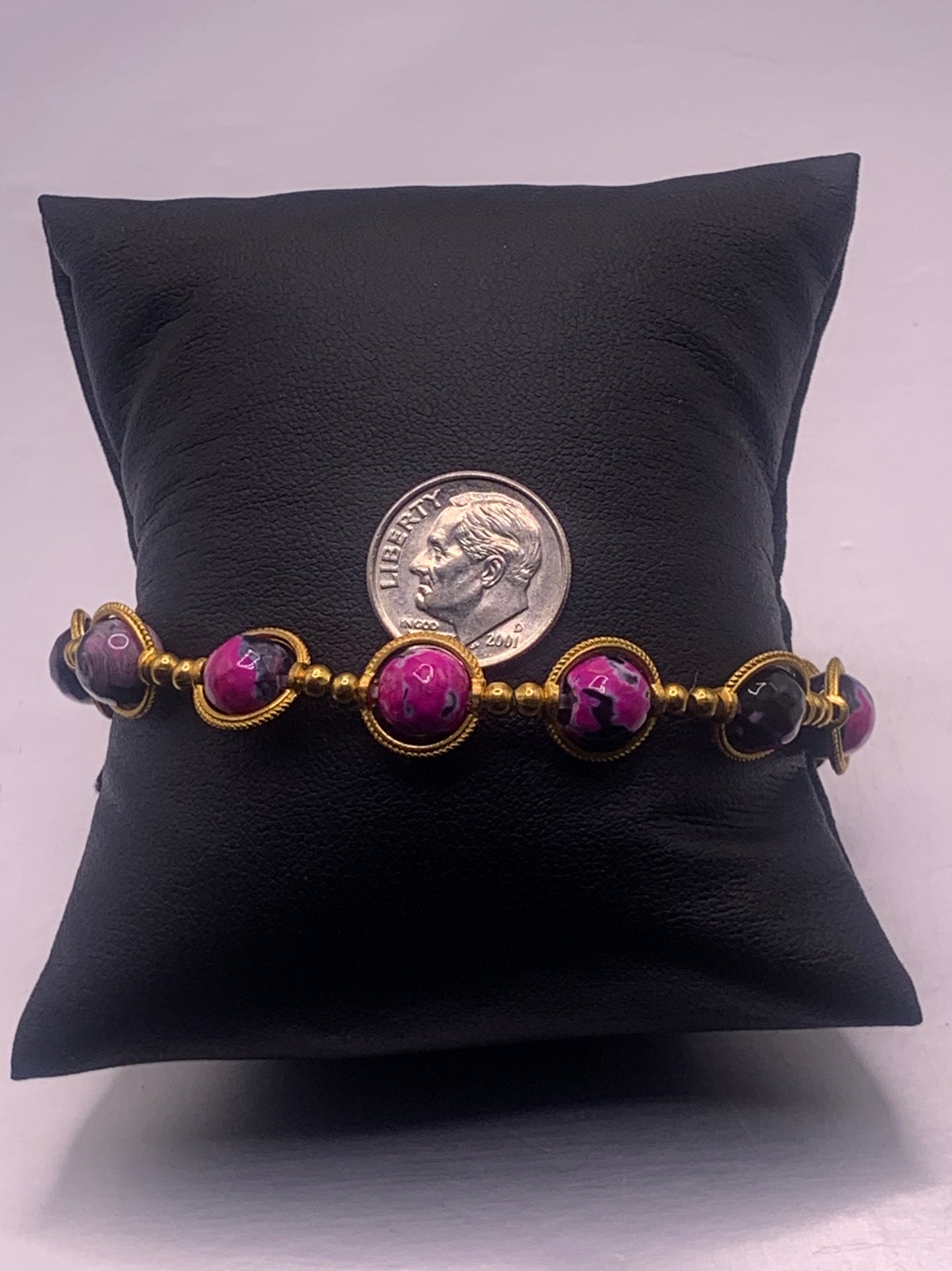 Bracelet with pink and black orca agate beads on a black pillow with a dime for scale