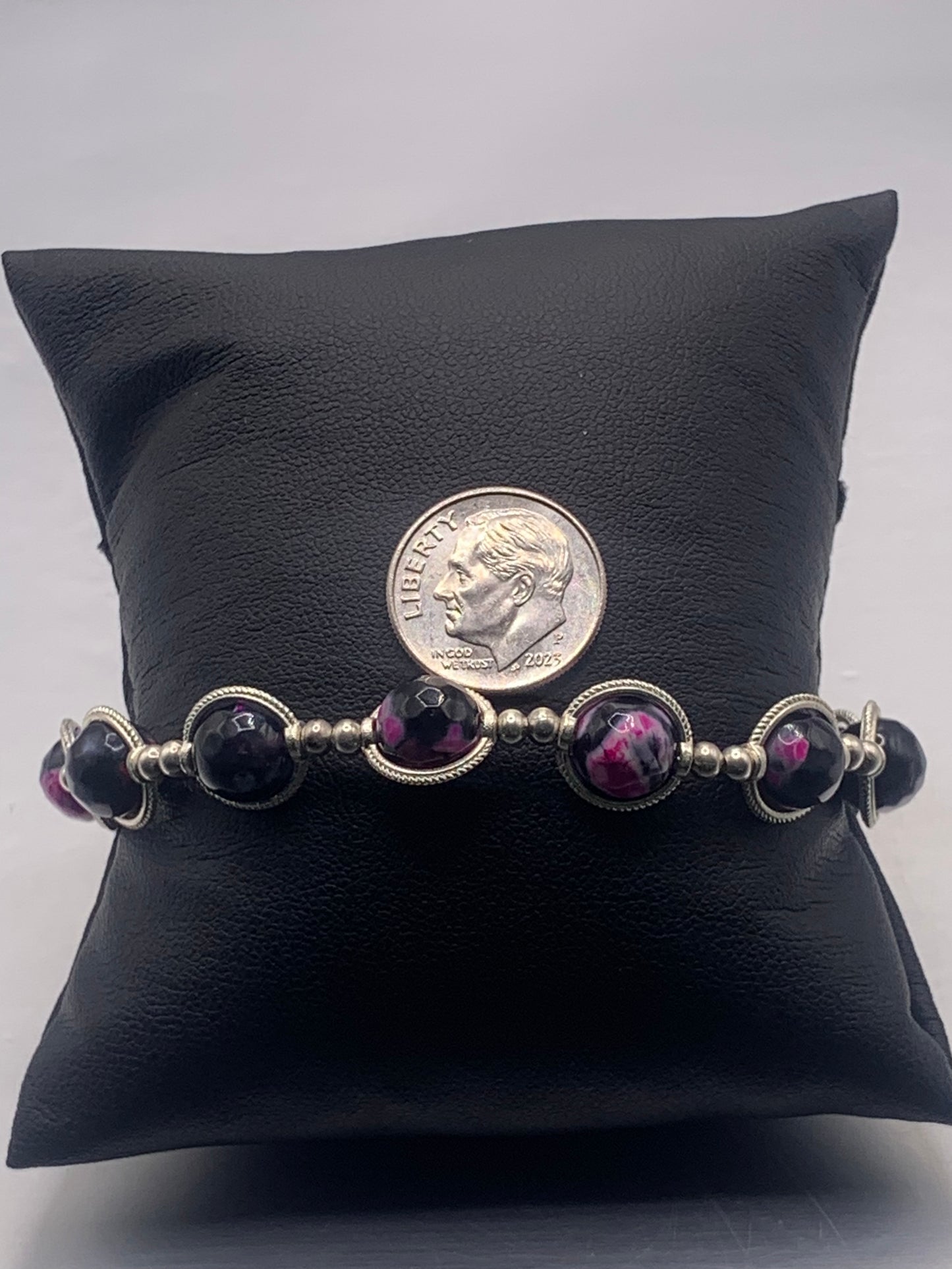 Bracelet with pink orca beads and silver accents on a black pillow with a dime for scale.