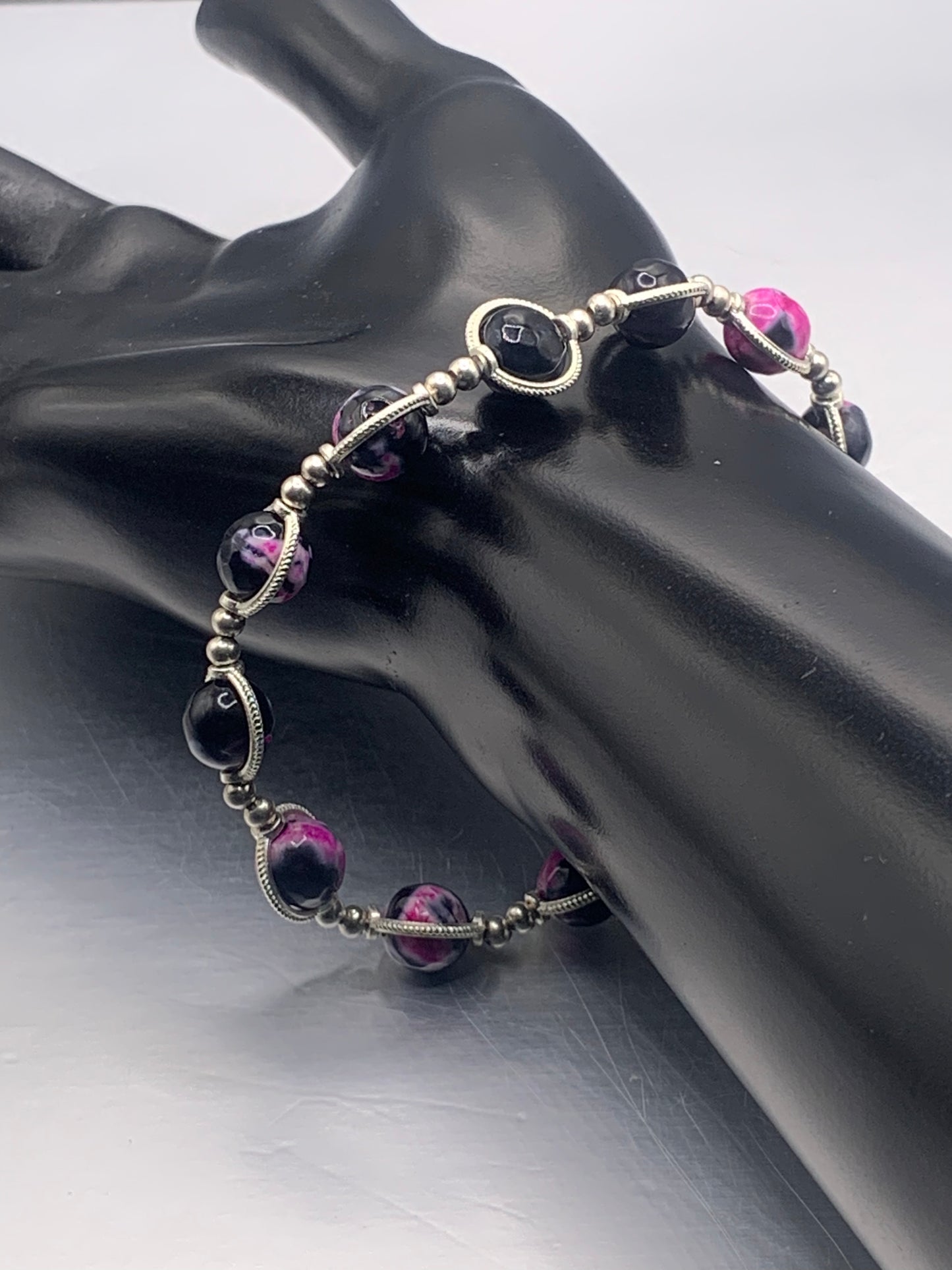 Bracelet with pink orca agate beads with silver accents on a black mannequin hand