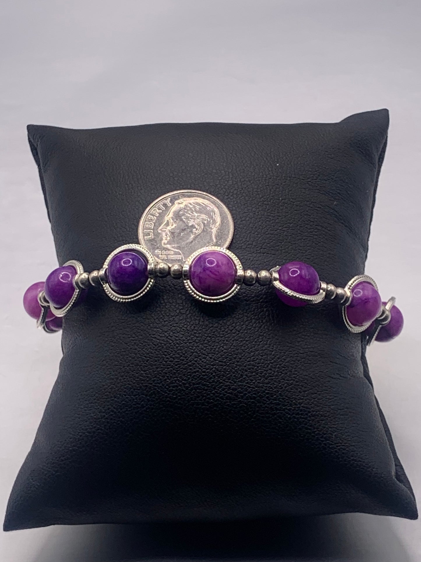 Purple charoite beaded bracelet on a black cushion with a coin for scale