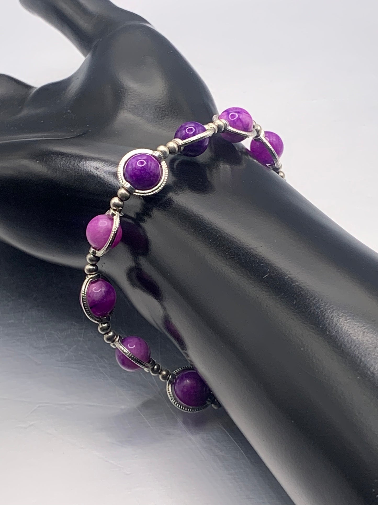 Purple charoite beaded bracelet on a black mannequin hand against a gray background