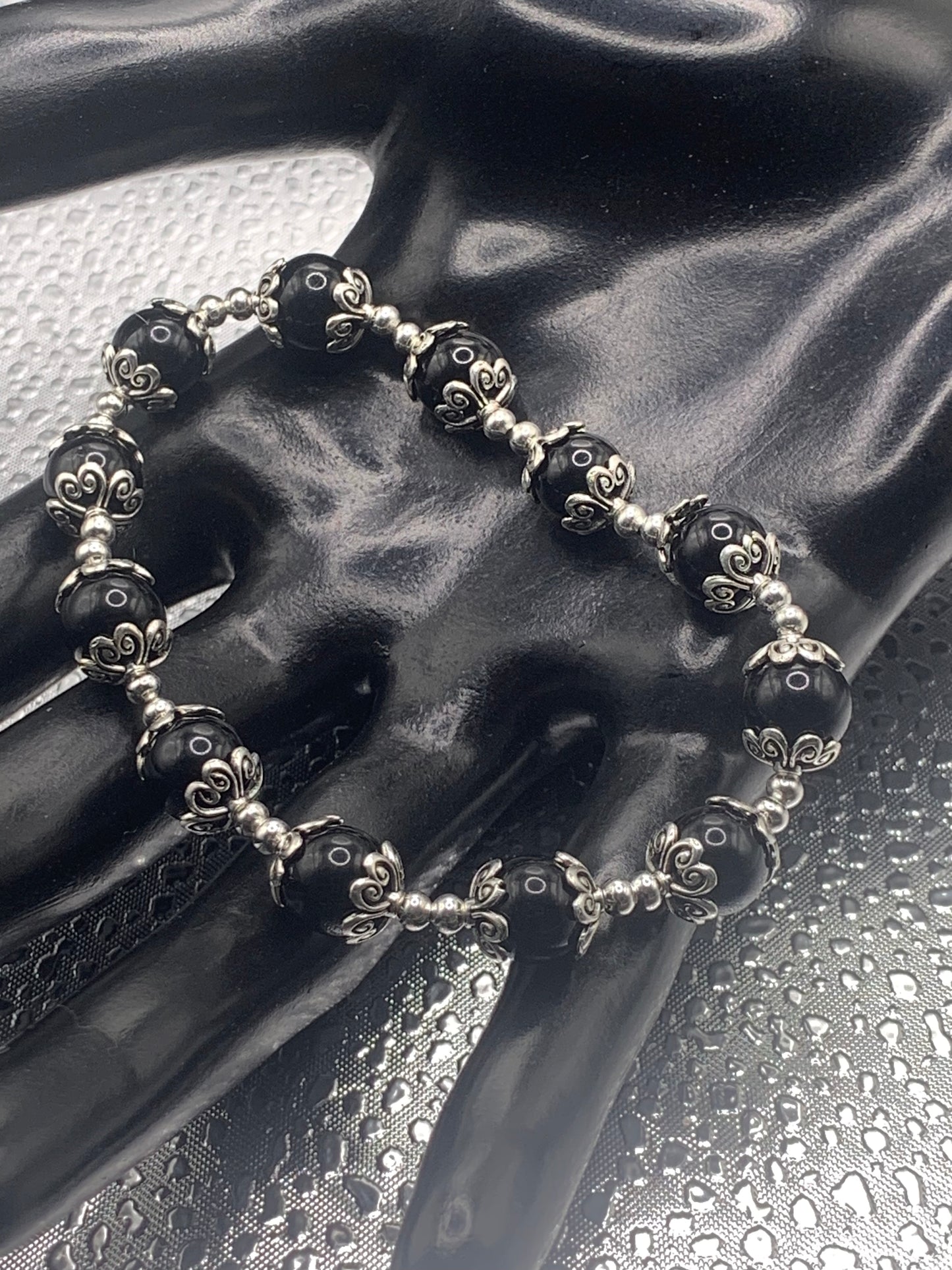 This bracelet contains black obsidian beads that are surrounded by bead caps and spacer beads