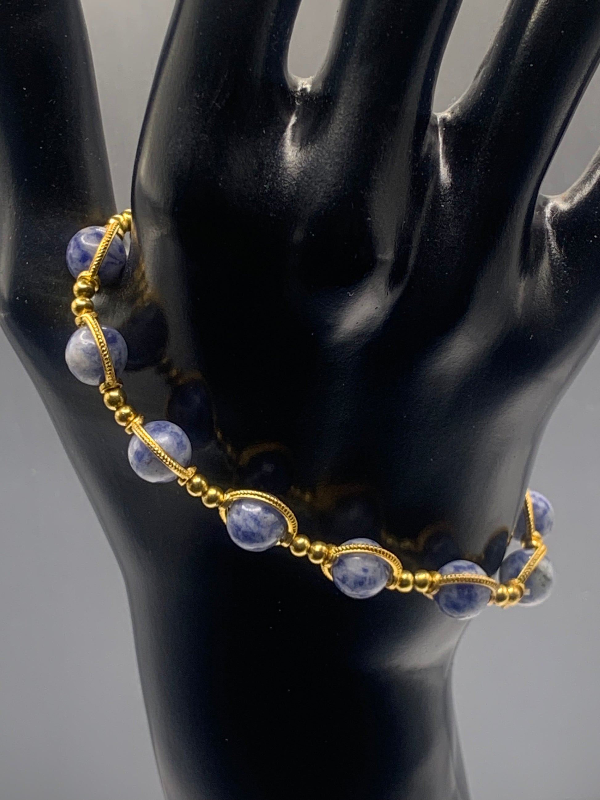 Gold bracelet with blue dot jasper beads on a black mannequin hand against a gray background
