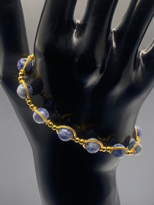 Gold bracelet with blue dot jasper beads on a black mannequin hand against a gray background
