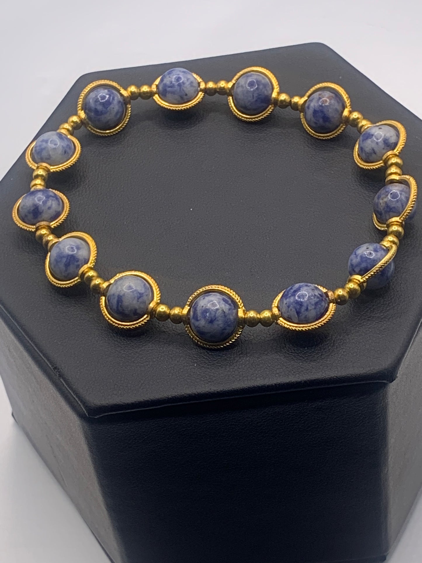 Bracelet with blue dot jasper beads and gold accents on a black hexagonal stand