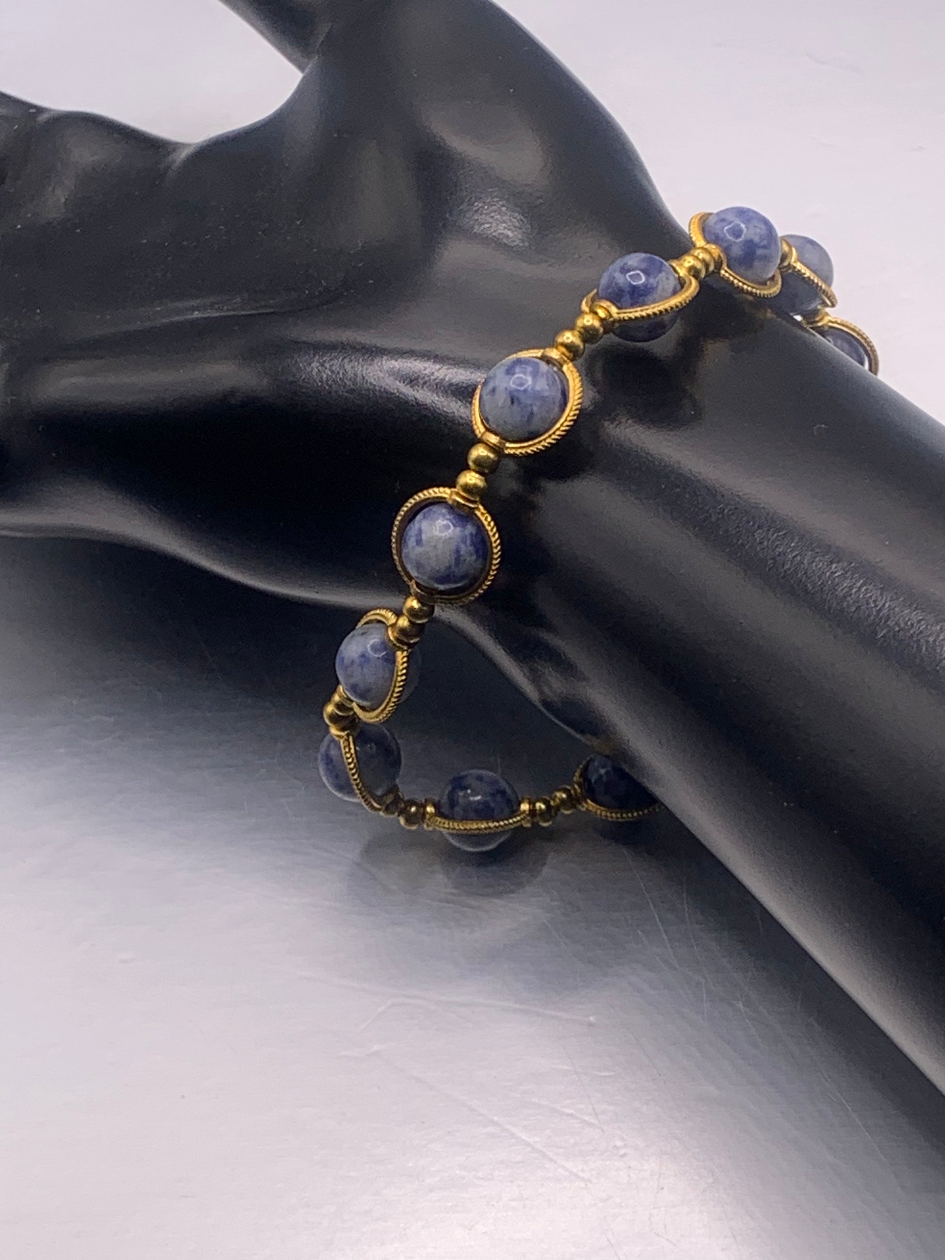 Bracelet with blue stones and gold accents on a black mannequin hand.