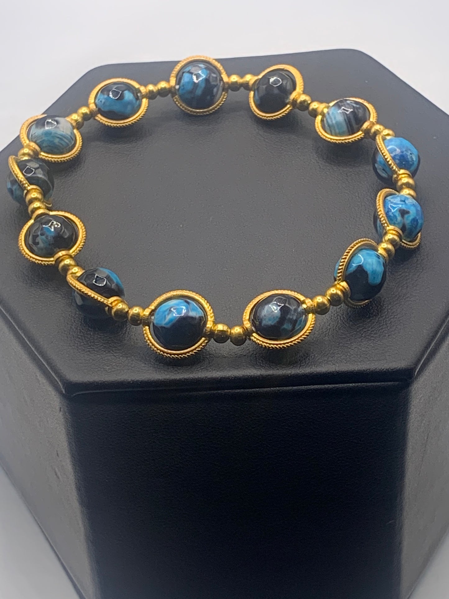 Bracelet with blue orca agate beads and gold accents on a black hexagonal stand