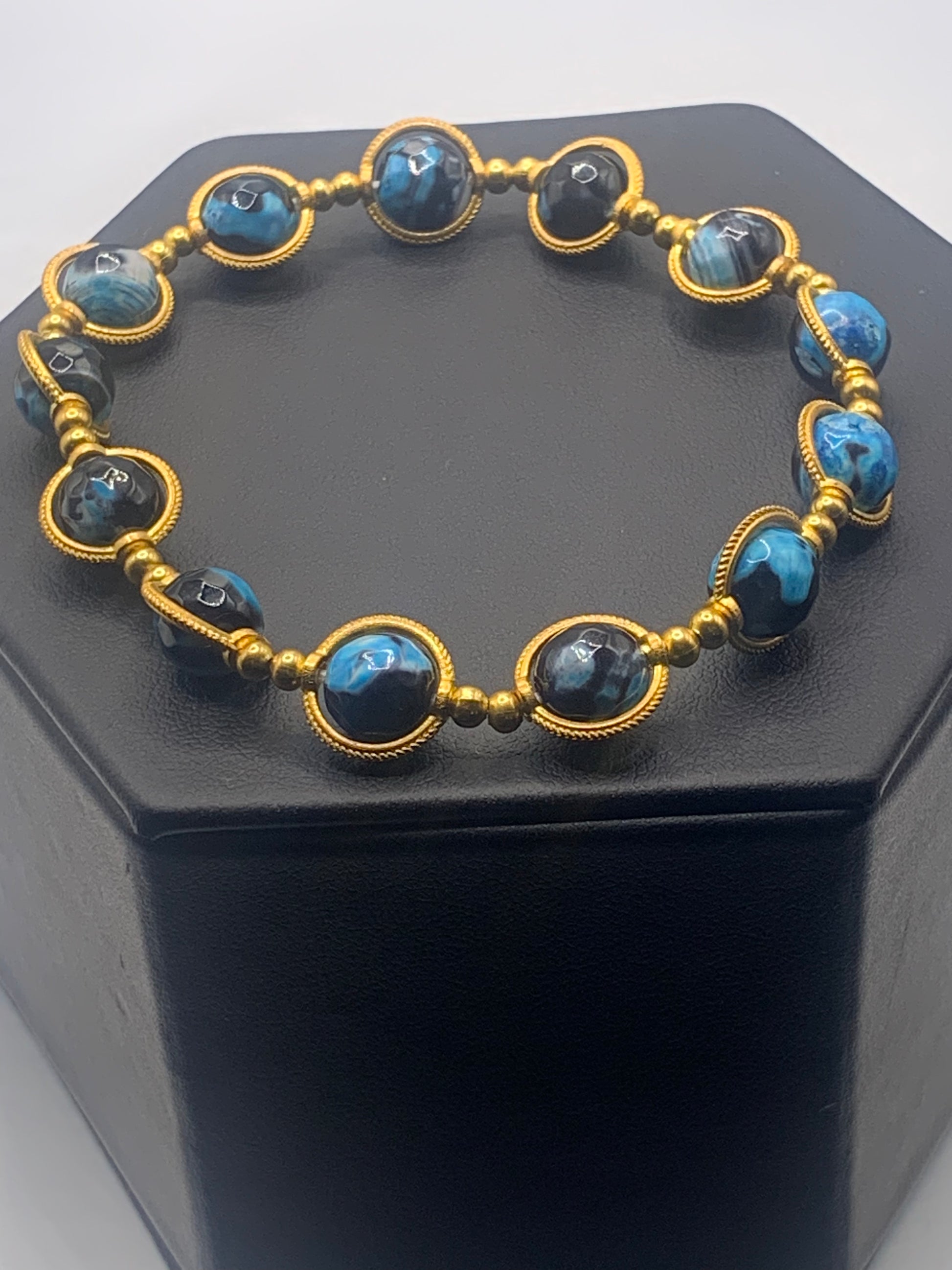 Bracelet with blue orca agate beads and gold accents on a black hexagonal stand