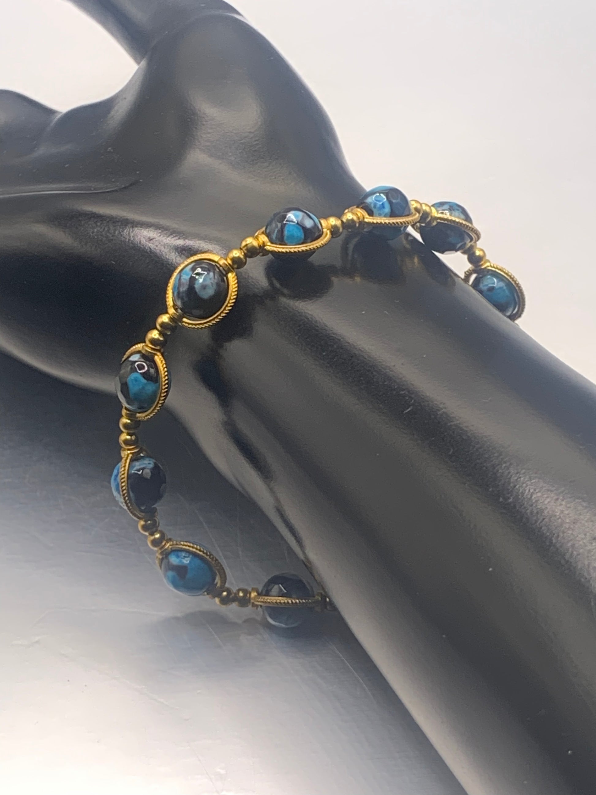Bracelet with blue orca agate beads and gold accents on a black mannequin hand.