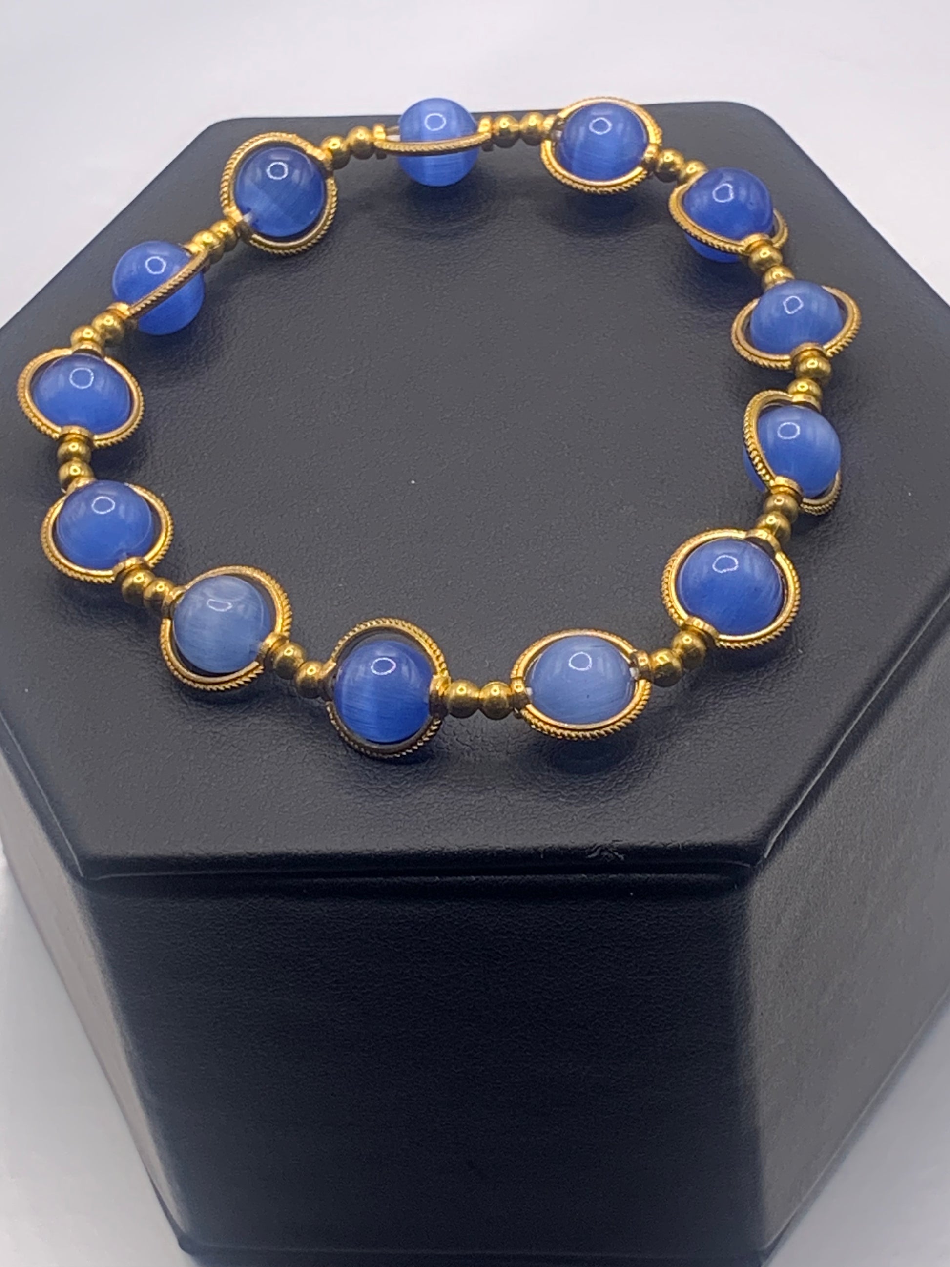 Bracelet with blue cats eye beads and gold accents on a black stand