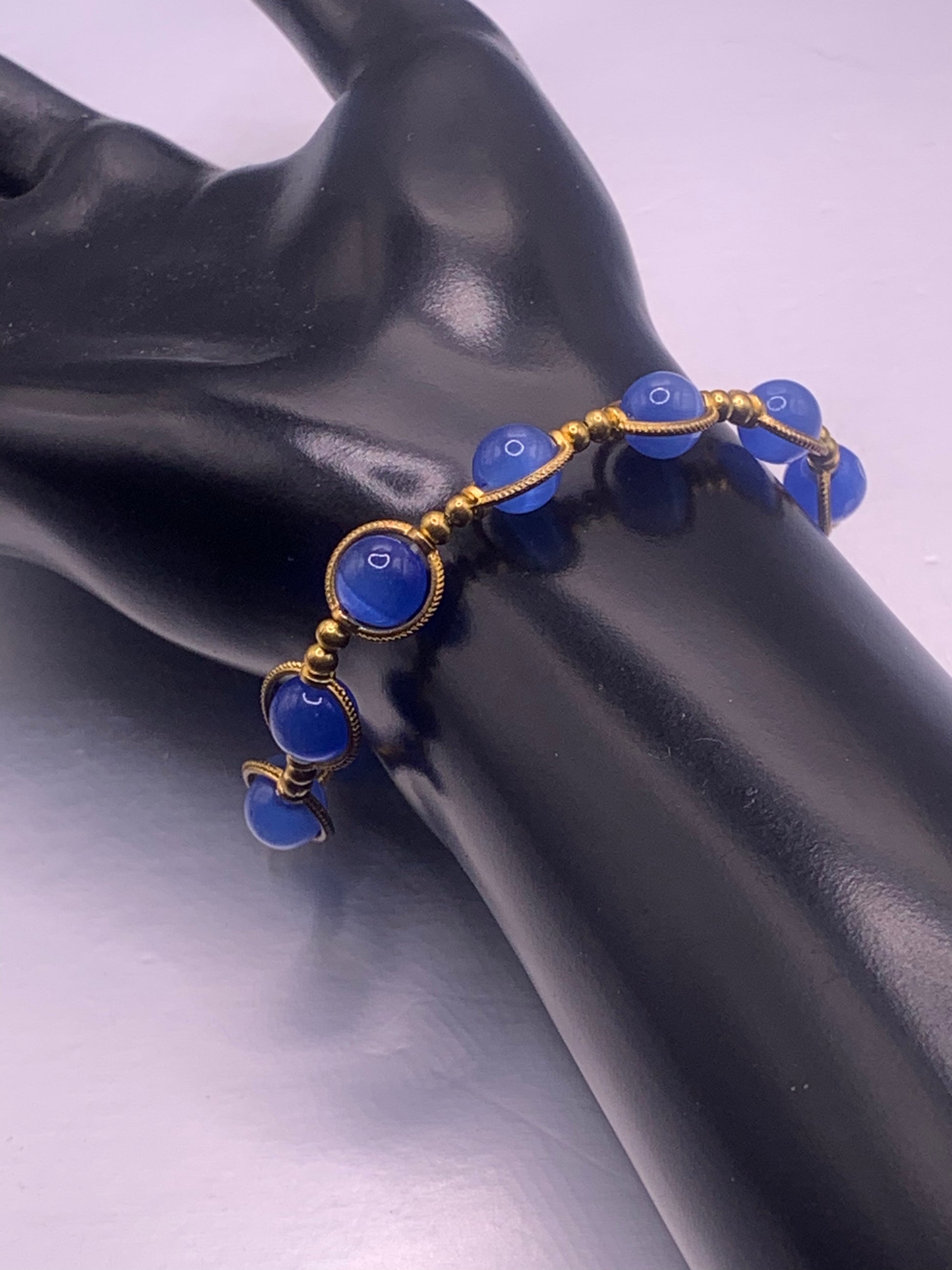 Blue cats eye beaded bracelet with gold accents on a black mannequin hand against a gray background
