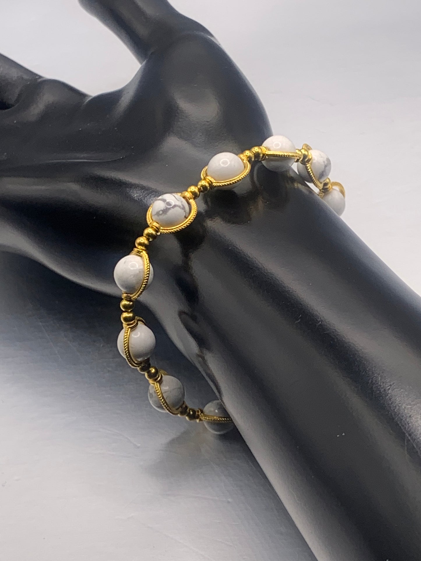 Bracelet with white howlite beads and gold accents on a black mannequin hand against a gray background