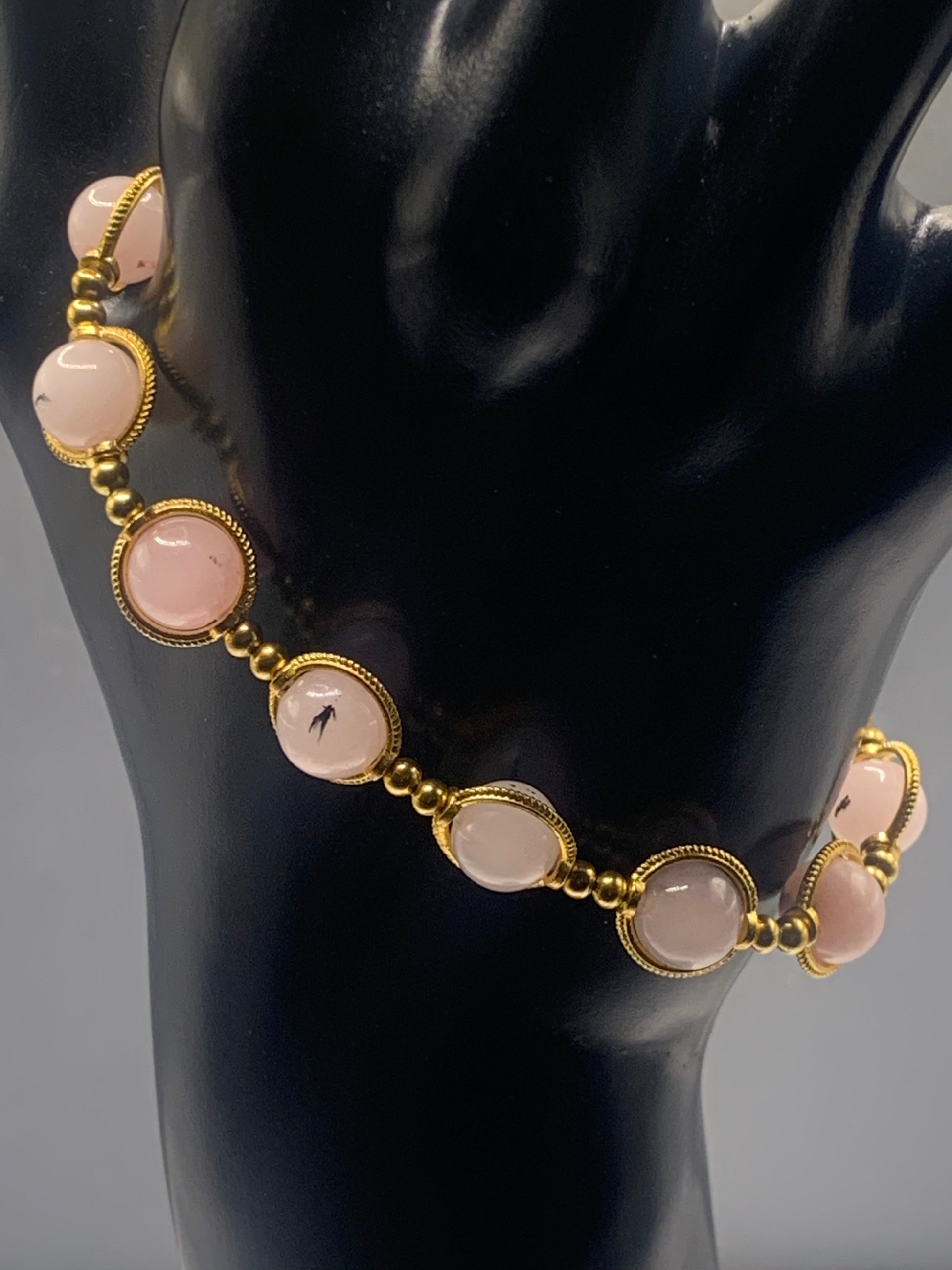 Bracelet with pink opal chalcedony beads and gold accents on a black mannequin.