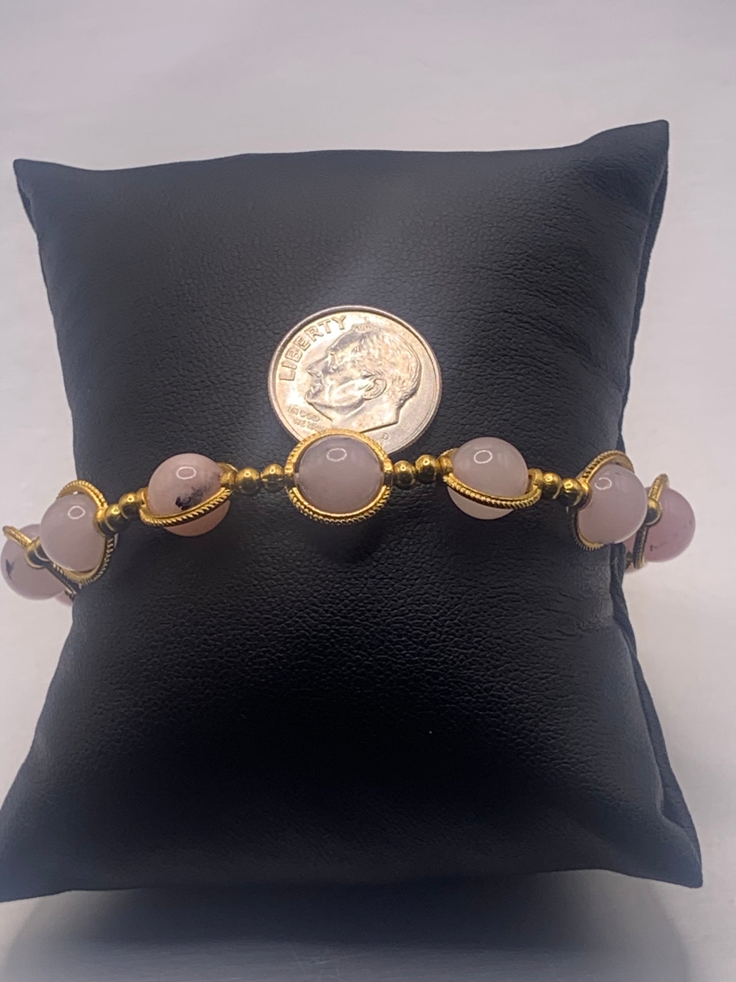 Bracelet with pink opal chalcedony beads on a black cushion with a coin for size comparrison