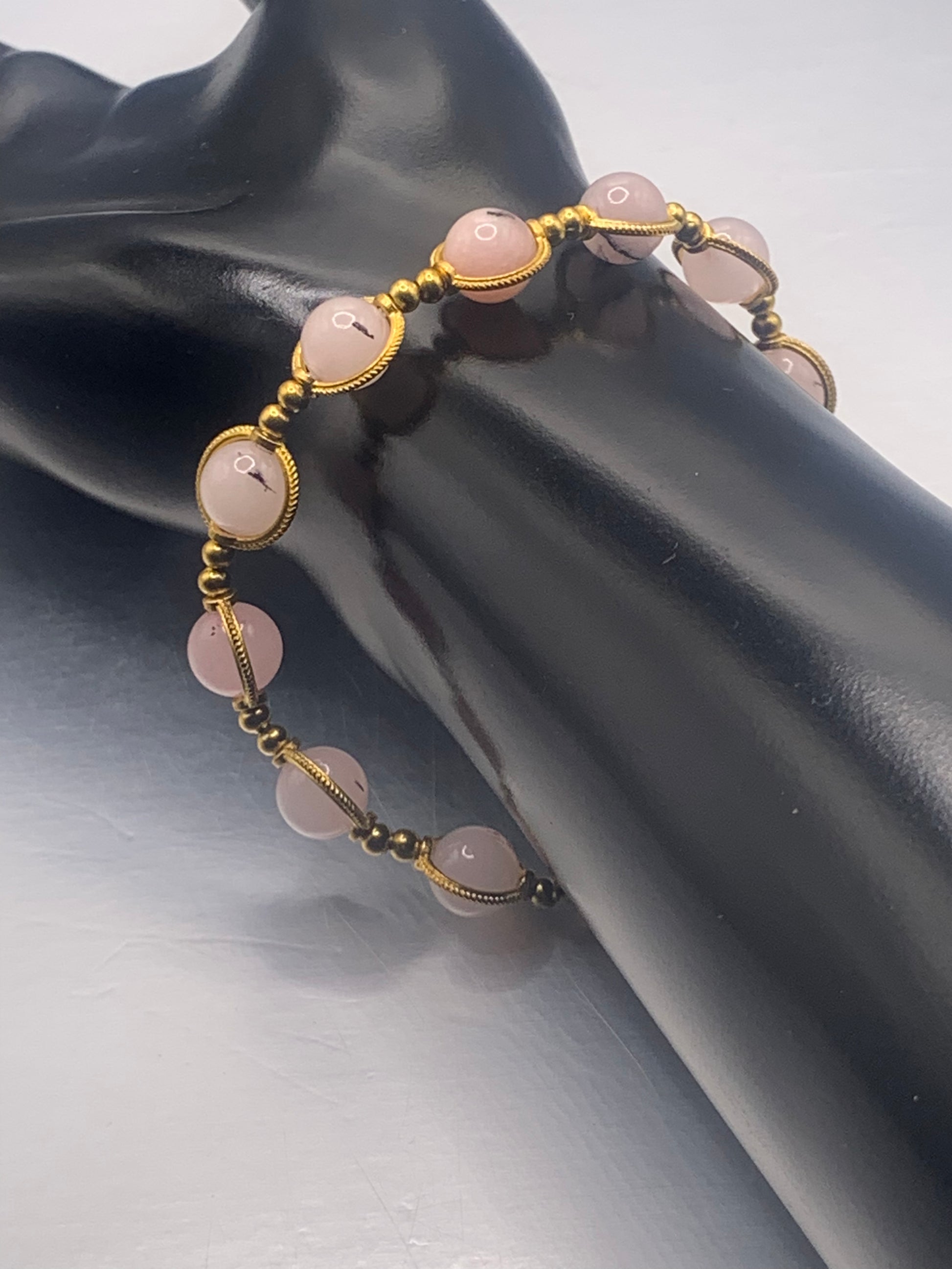 Bracelet with pink opal chalcedony beads and gold accents on a black mannequin arm.