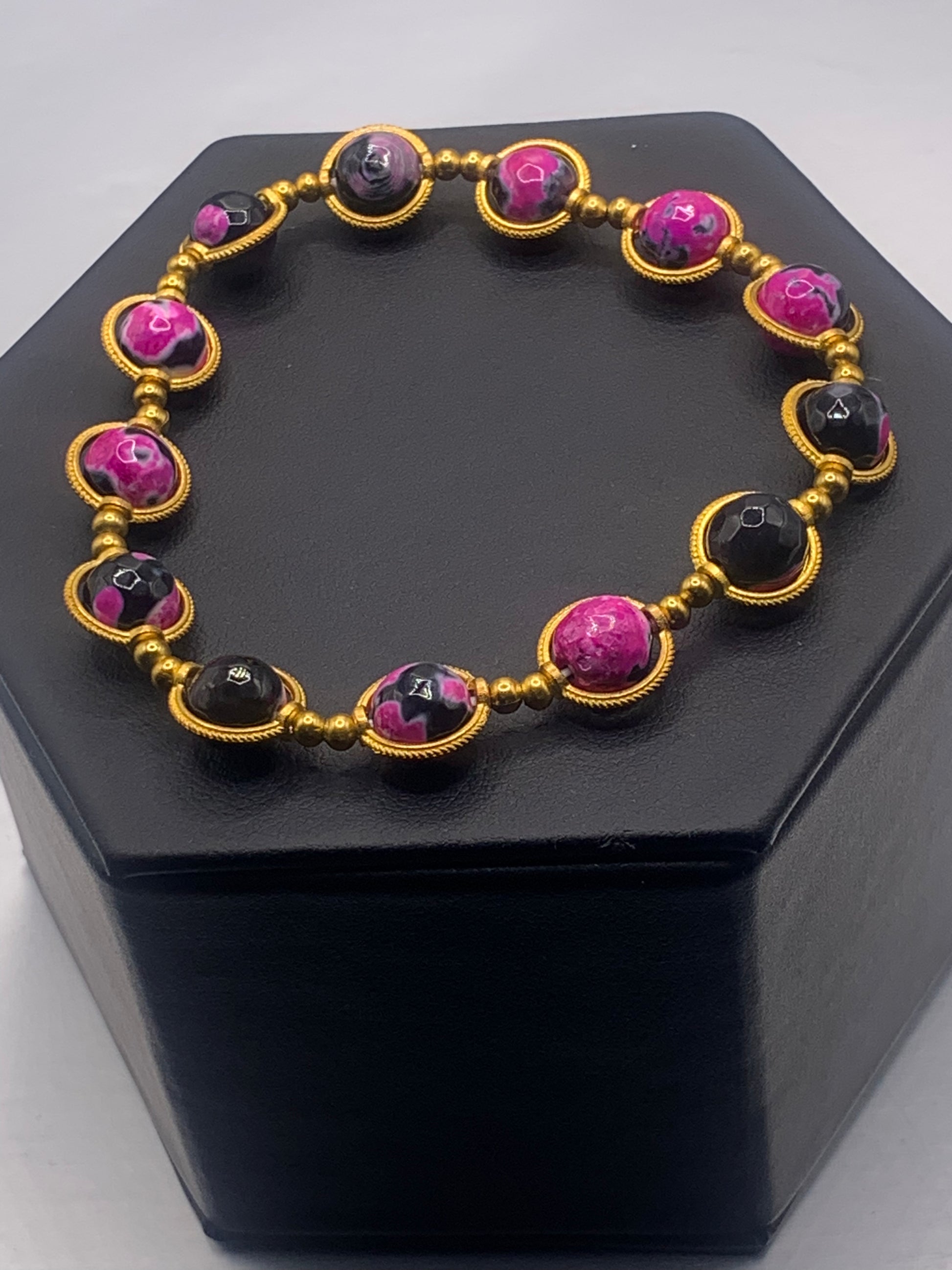 Bracelet with pink and black orca agate beads on a black hexagonal stand