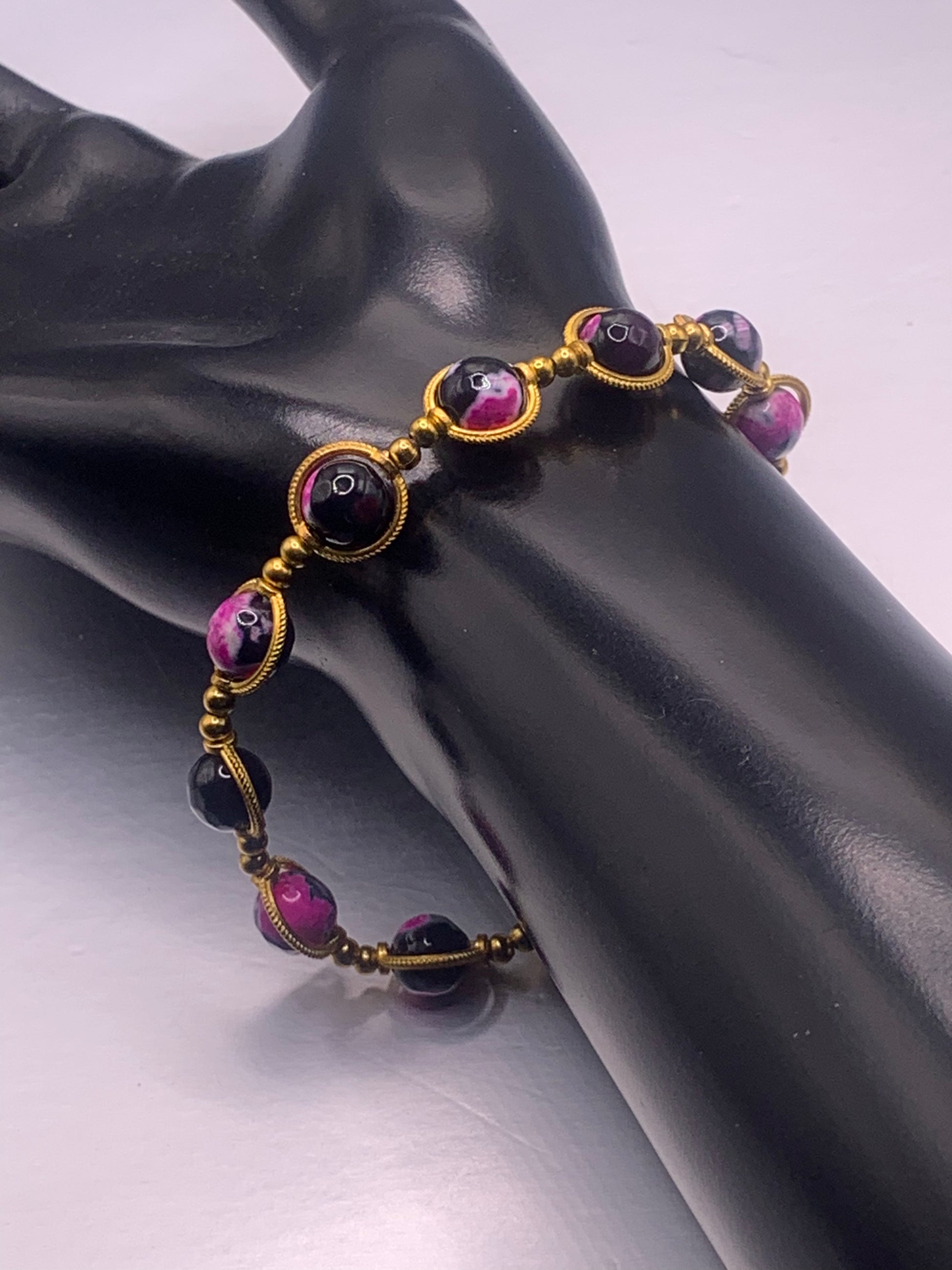Bracelet with pink and black orca agate beads with gold accents on a black mannequin hand