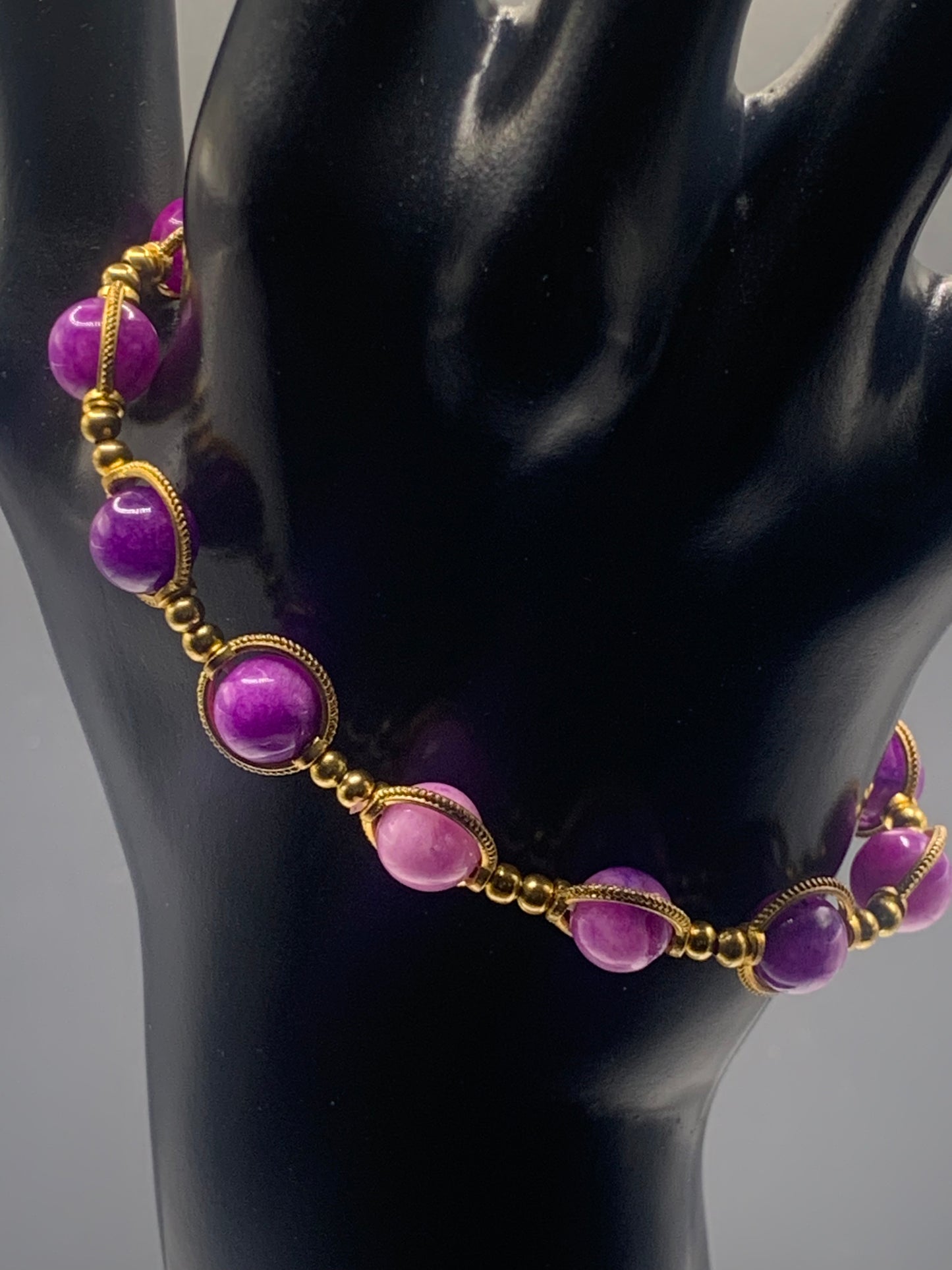 Necklace with purple charoite beads and gold accents on a black mannequin.
