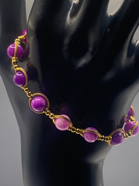 Necklace with purple charoite beads and gold accents on a black mannequin.
