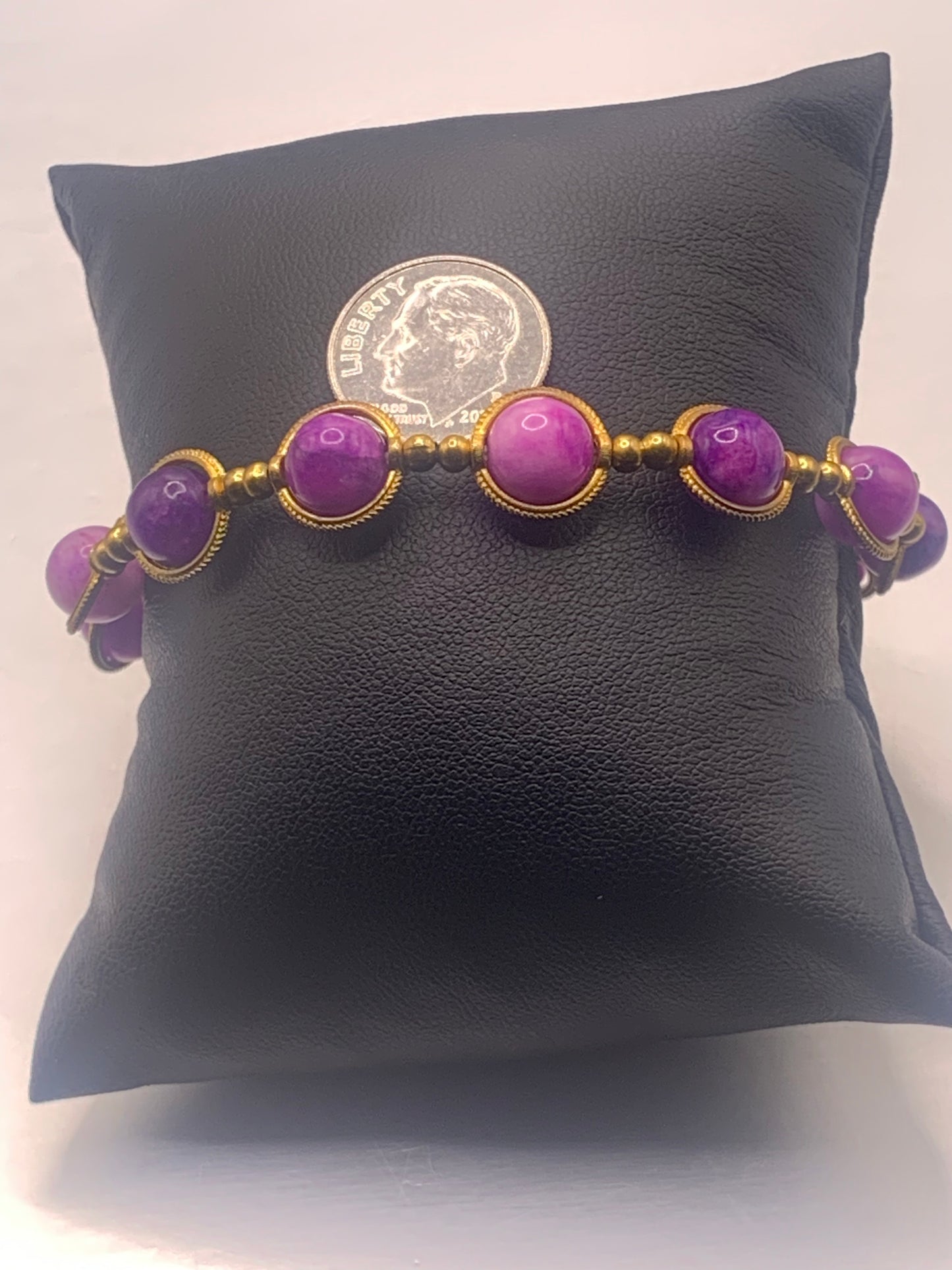 Purple charoite beaded bracelet with gold accents on a black cushion, next to a coin for scale.