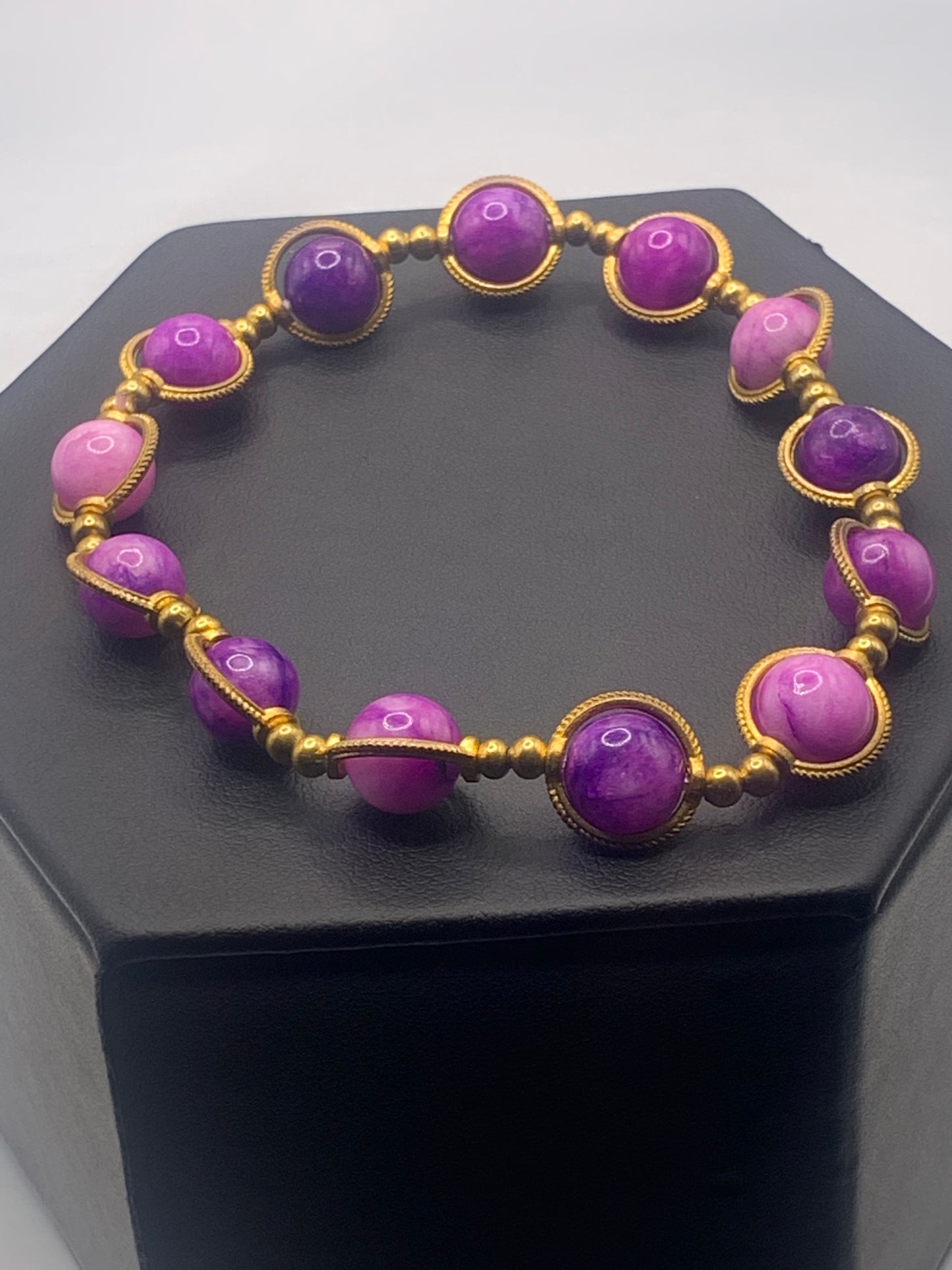 Purple charoite beaded bracelet with gold accents on a black stand
