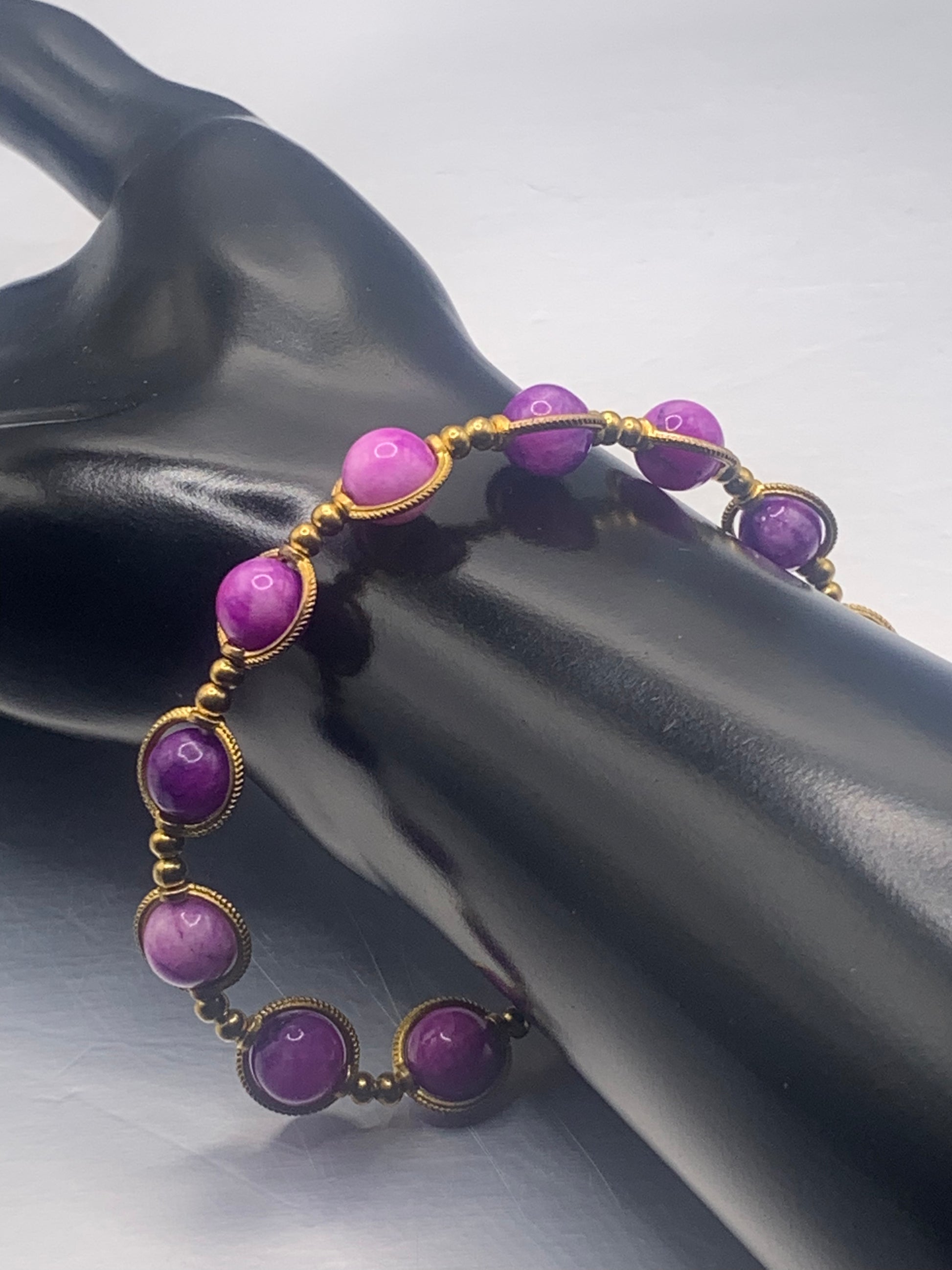 Purple charoite beaded bracelet with gold accents on a mannequin hand against a gray background