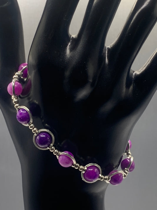 Purple charoite beaded bracelet on a black mannequin hand against a gray background