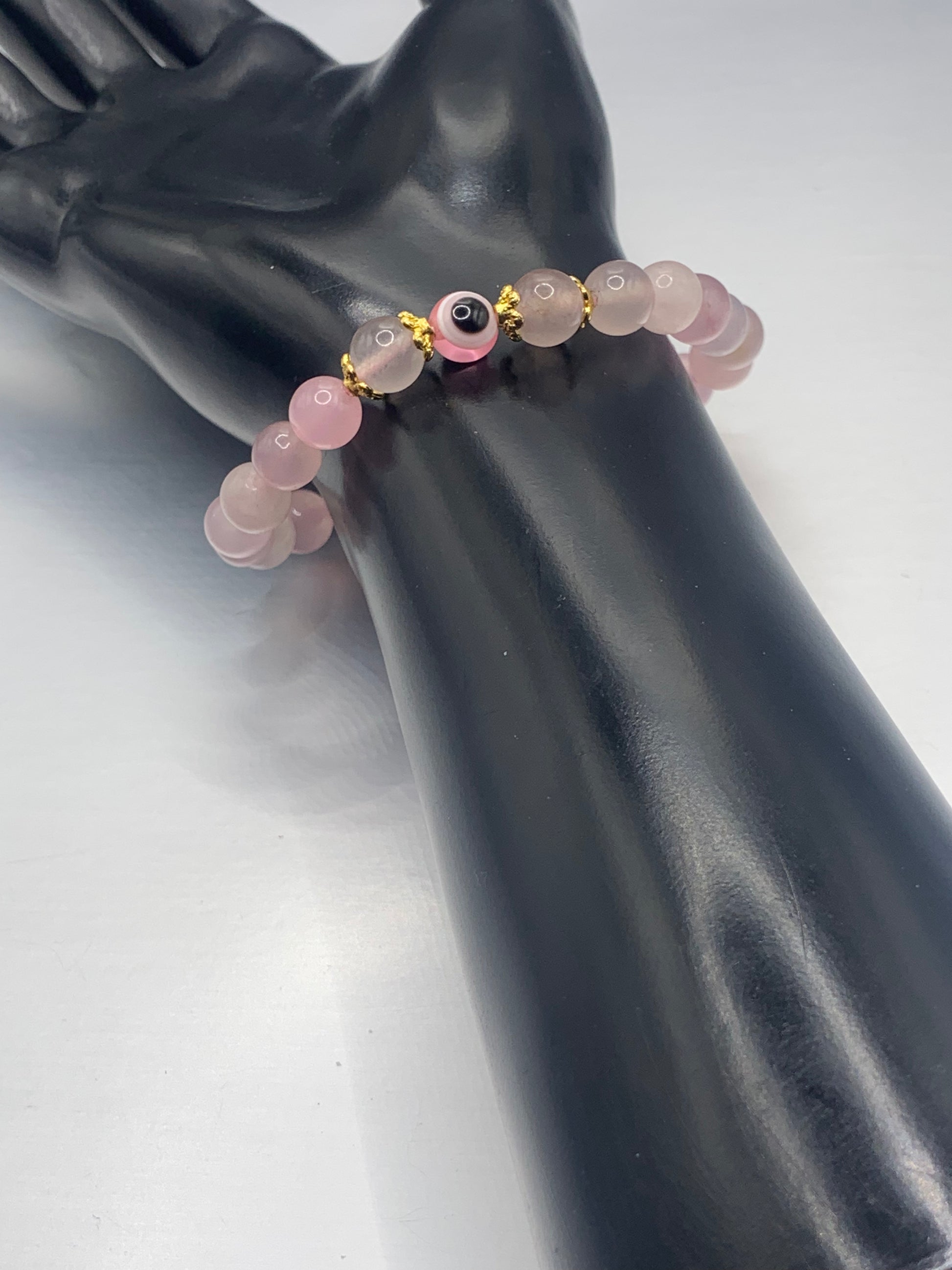 This bracelet features rose quartz (enhanced) beads with a resin evil eye as the focal bead. Each bead on either side of the evil eye have bead caps to draw attention to the evil eye bead. This picture is taken with the bracelet being worn on a wrist 