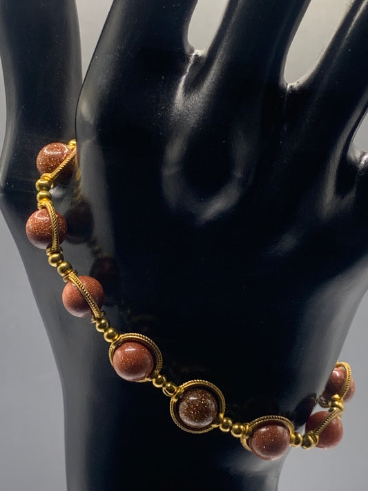 Bracelet with sandstone beads and gold accents on a black mannequin hand.