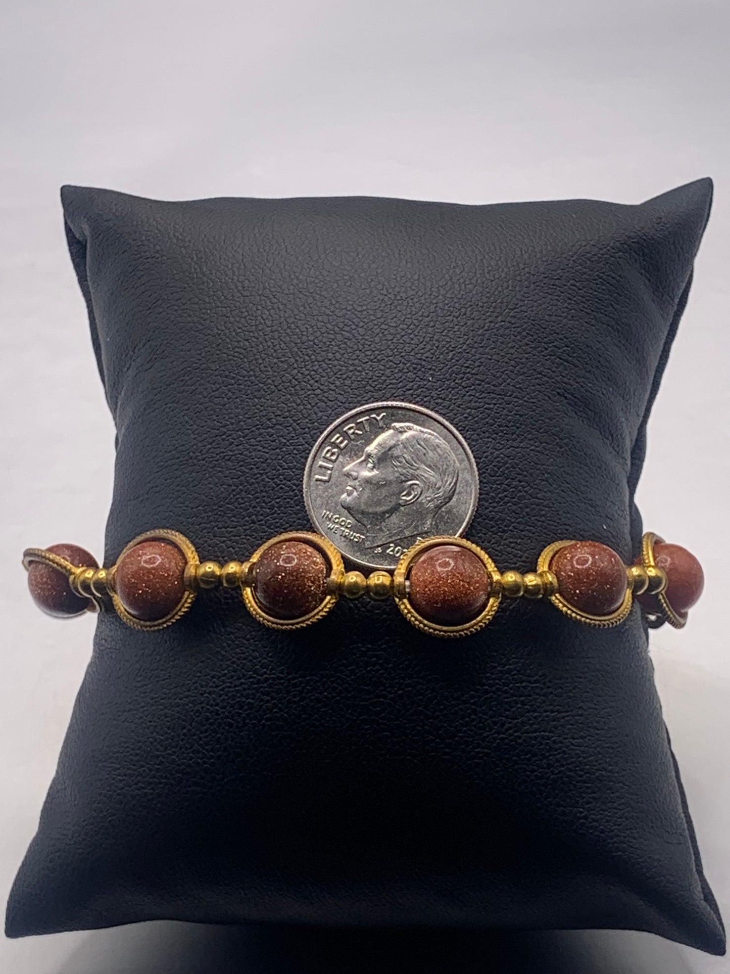 Bracelet with sandstone beads and gold accents on a black pillow with a dime for scale.