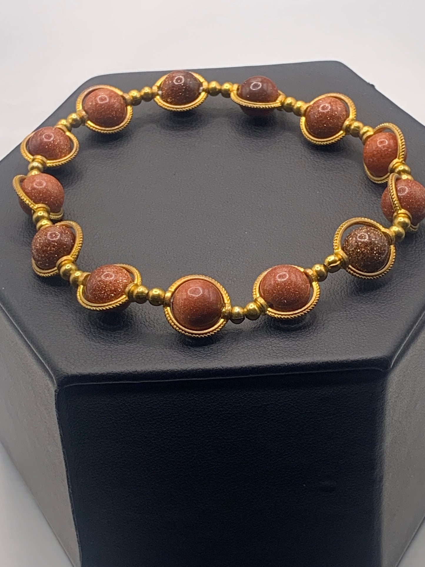 Bracelet with sandstone beads and gold accents on a black hexagonal stand