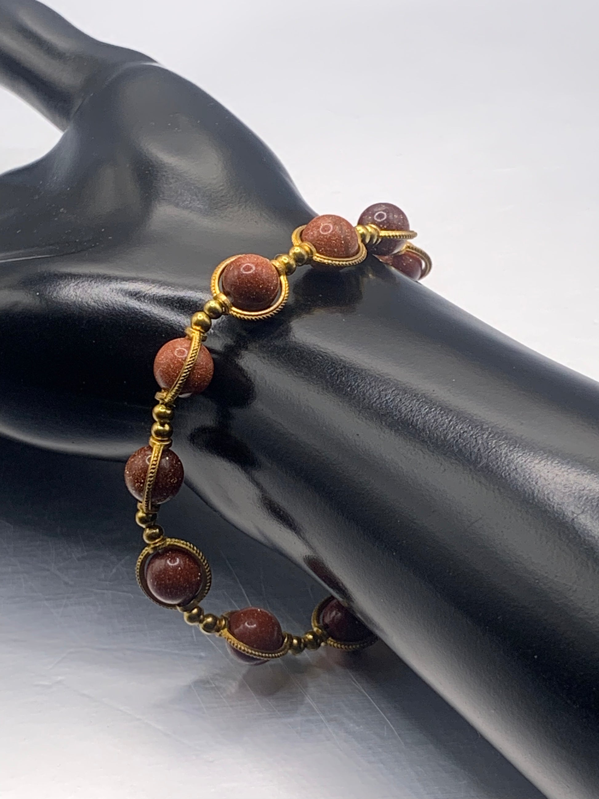 Bracelet with sandstone beads and gold accents on a black mannequin hand.