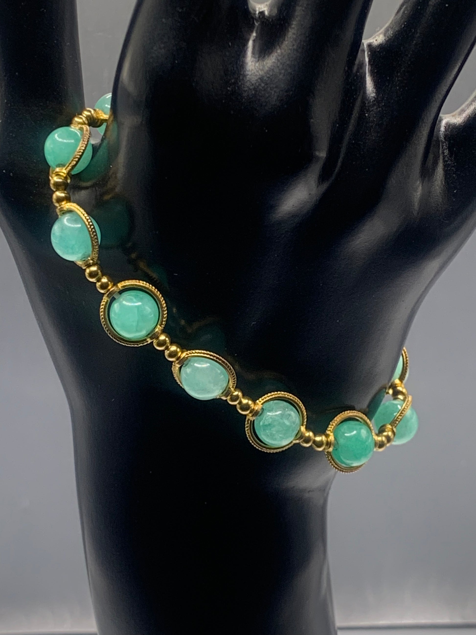 Bracelet with teal chalcedony beads and gold accents on a black mannequin hand
