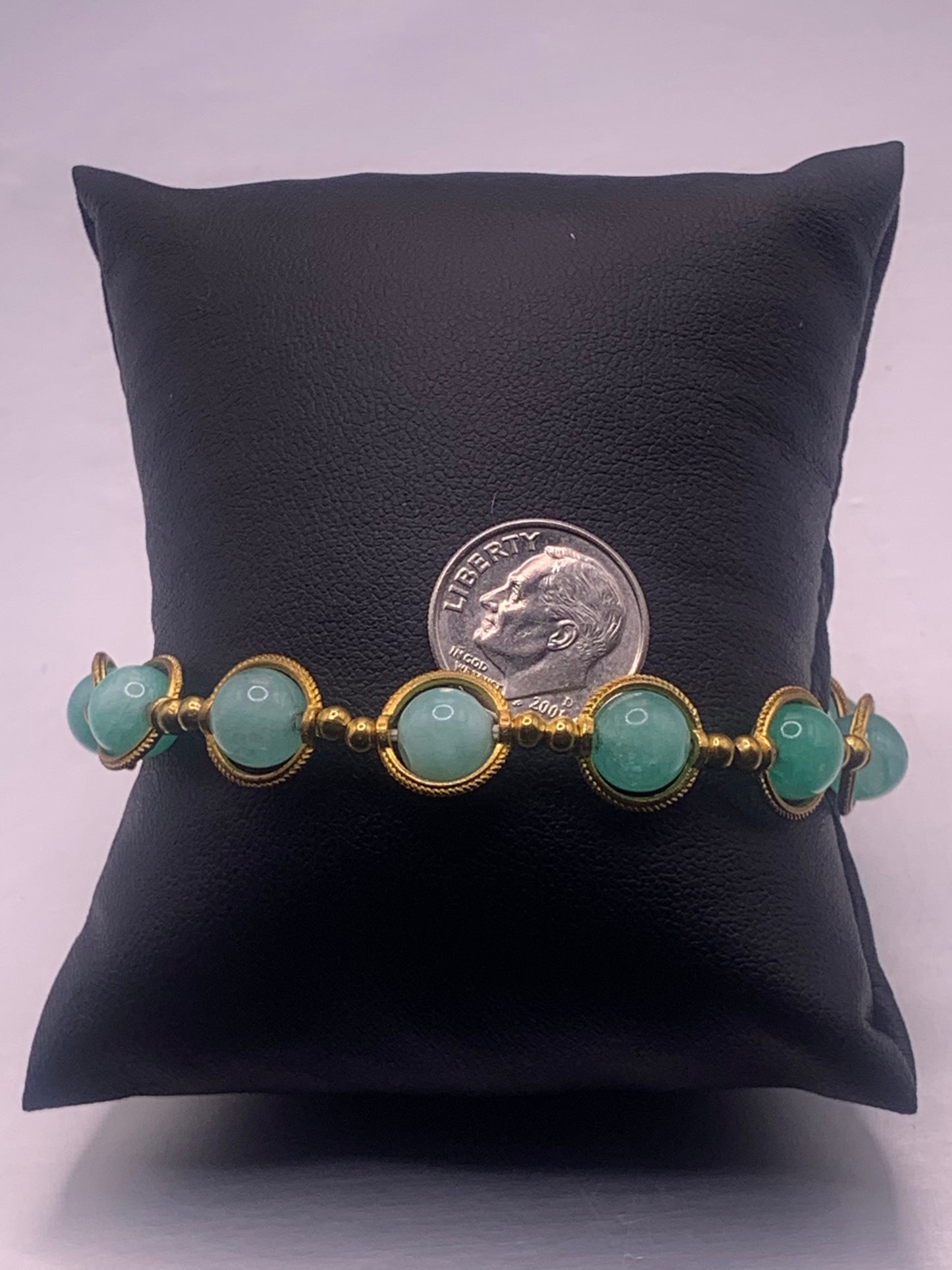 Bracelet with teal chalcedony beads and gold accents on a black pillow with a dime for scale.
