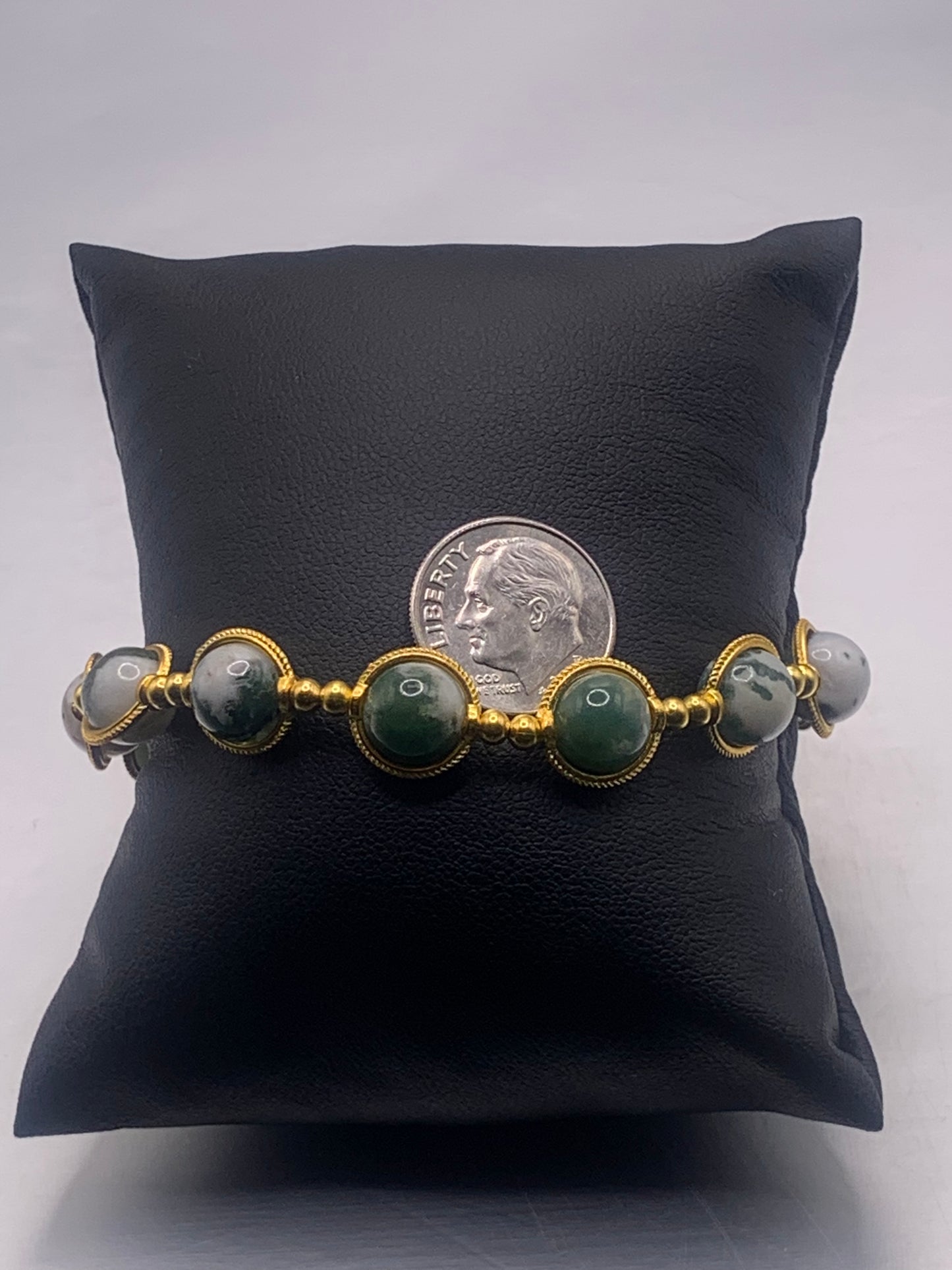 Bracelet with tree moss agate beads and gold accents on a black cushion, with a dime for scale.