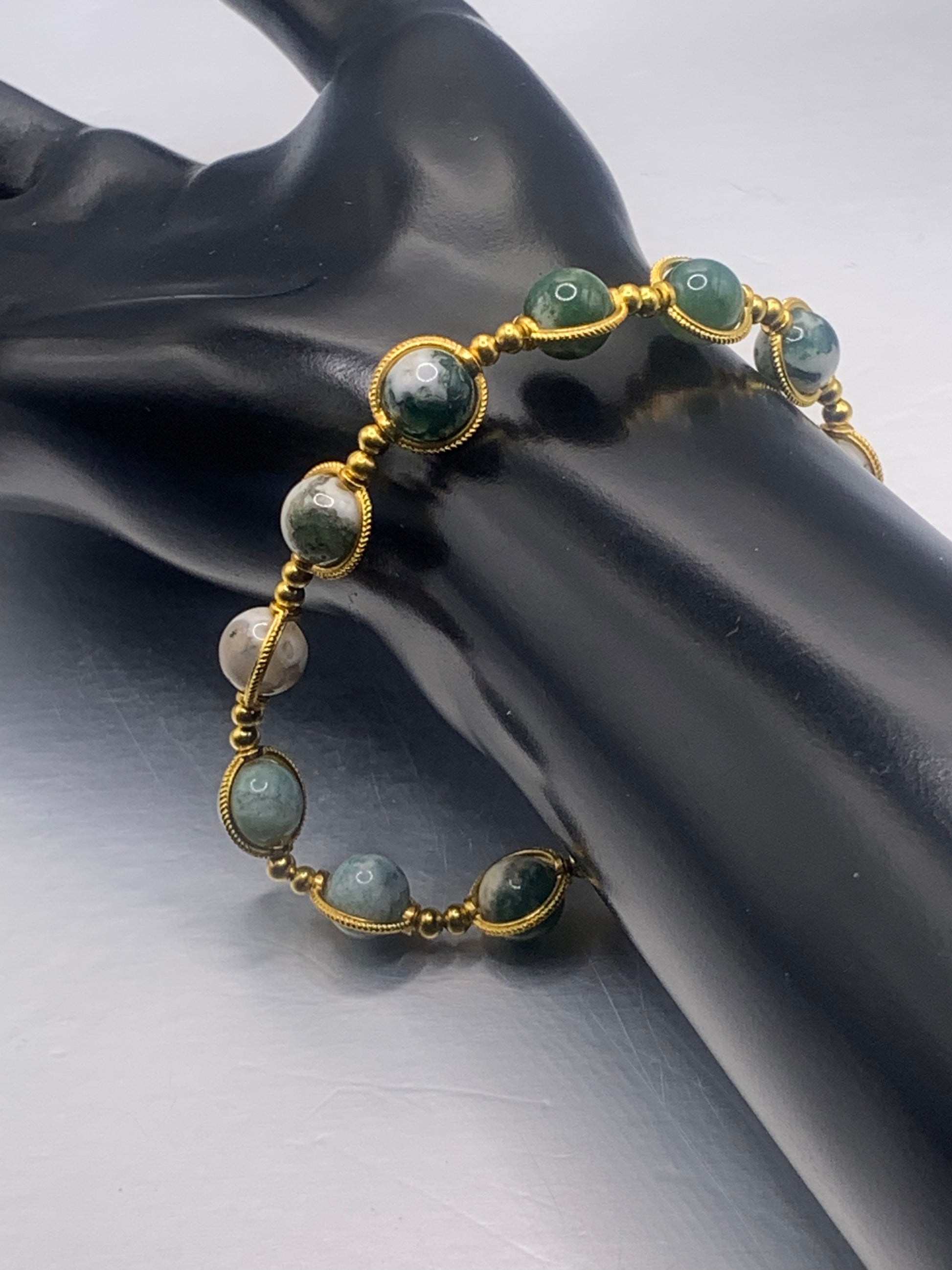 Bracelet with tree moss agate beads and gold accents on a black mannequin hand against a gray background