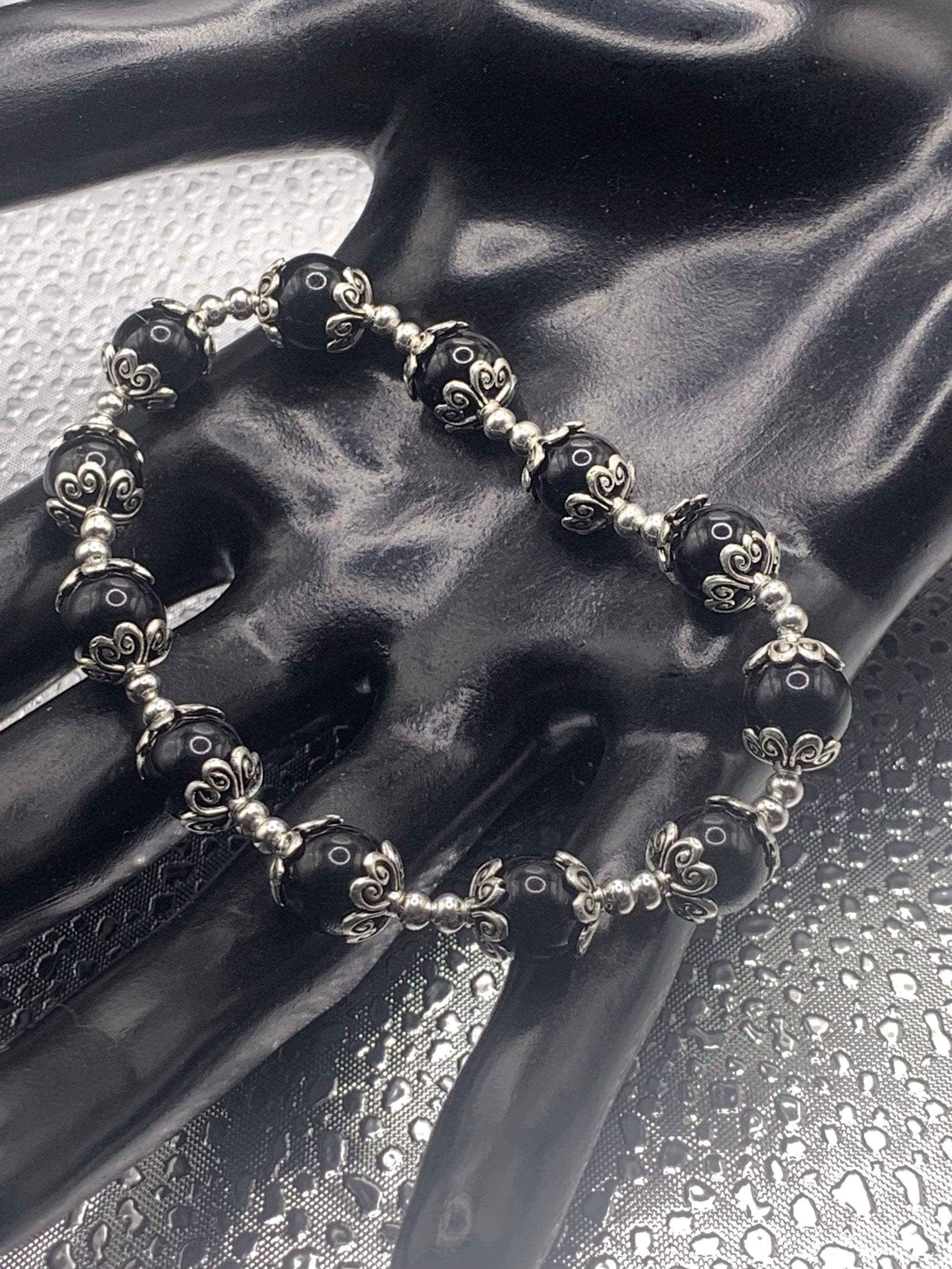 This bracelet contains black obsidian beads that are surrounded by bead caps and spacer beads