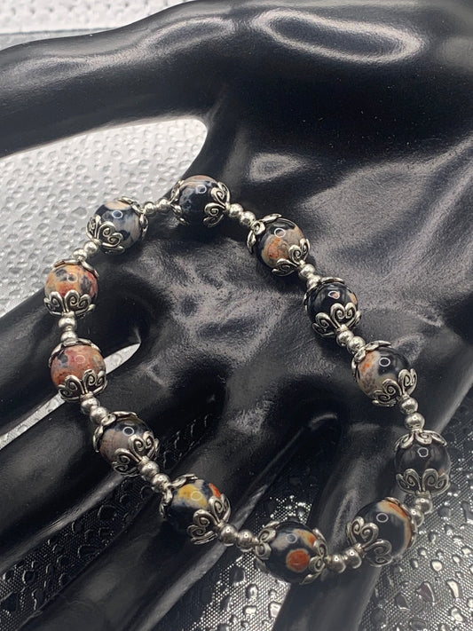 This bracelet contains orange orca agate beads that are surrounded by bead caps and spacer beads
