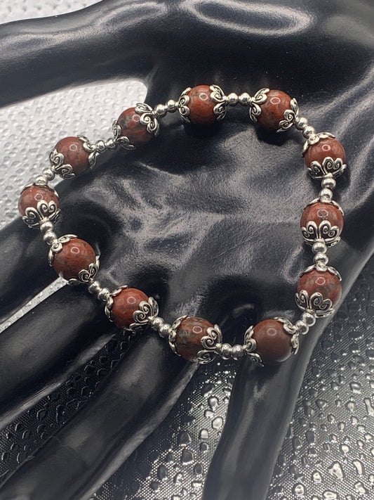 This bracelet contains red sesame jasper beads that are surrounded by bead caps and spacer beads