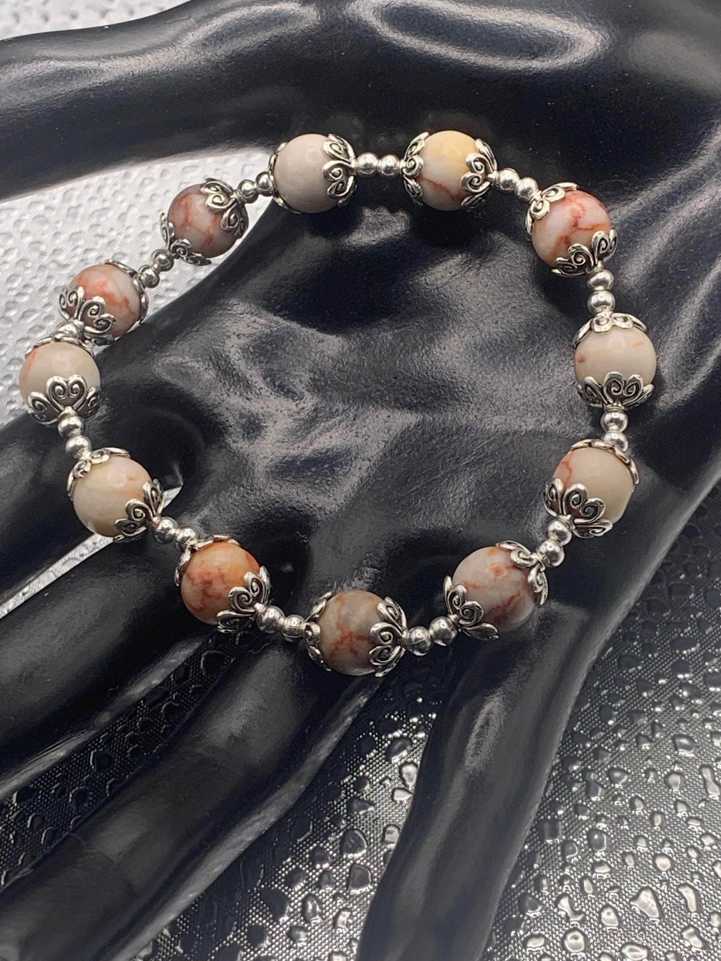 This bracelet contains red vein jasper beads that are surrounded by bead caps and spacer beads
